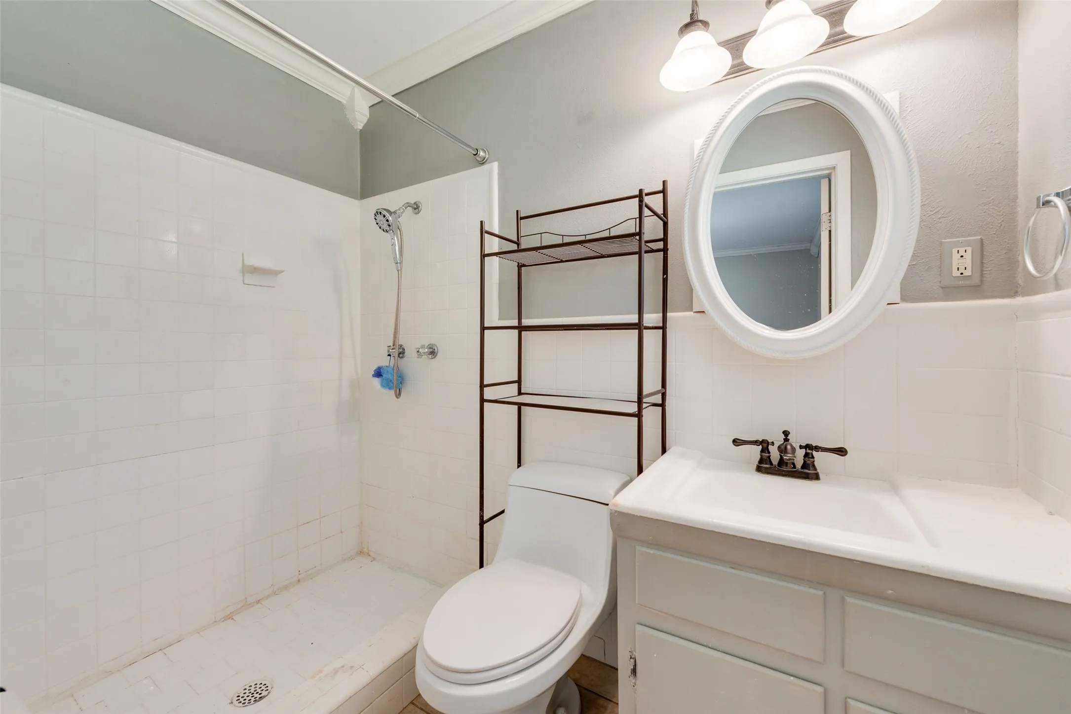 Bathroom featuring a white vanity with an integrated sink, dual-handle metal faucet, oval wall-mounted mirror, and a tub-shower combination with white wall tile