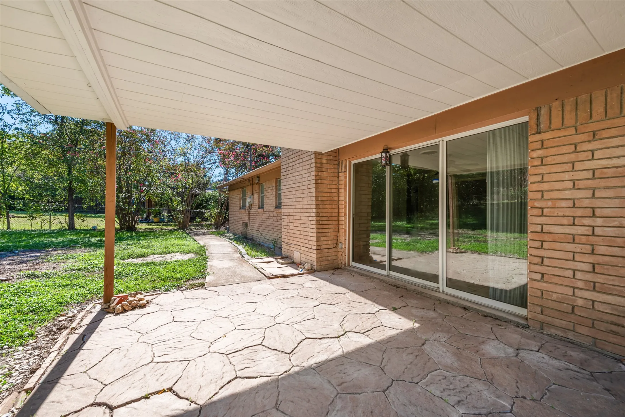 Covered patio featuring a flagstone-patterned concrete surface, brick exterior masonry, and large sliding glass doors