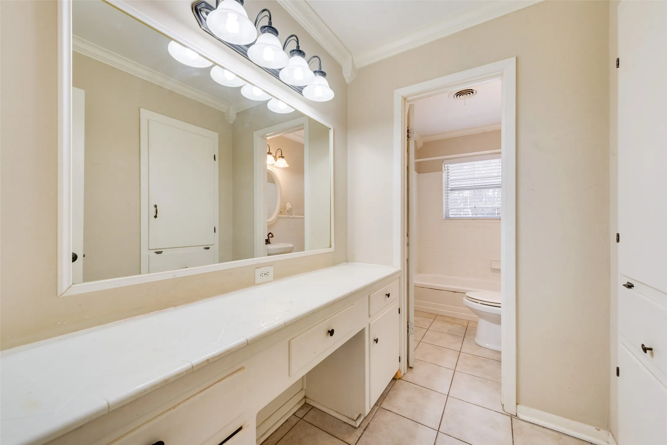Bathroom vanity featuring a tiled countertop, large wall-mounted mirror, multi-bulb light fixture, built-in cabinetry, and ceramic tile flooring