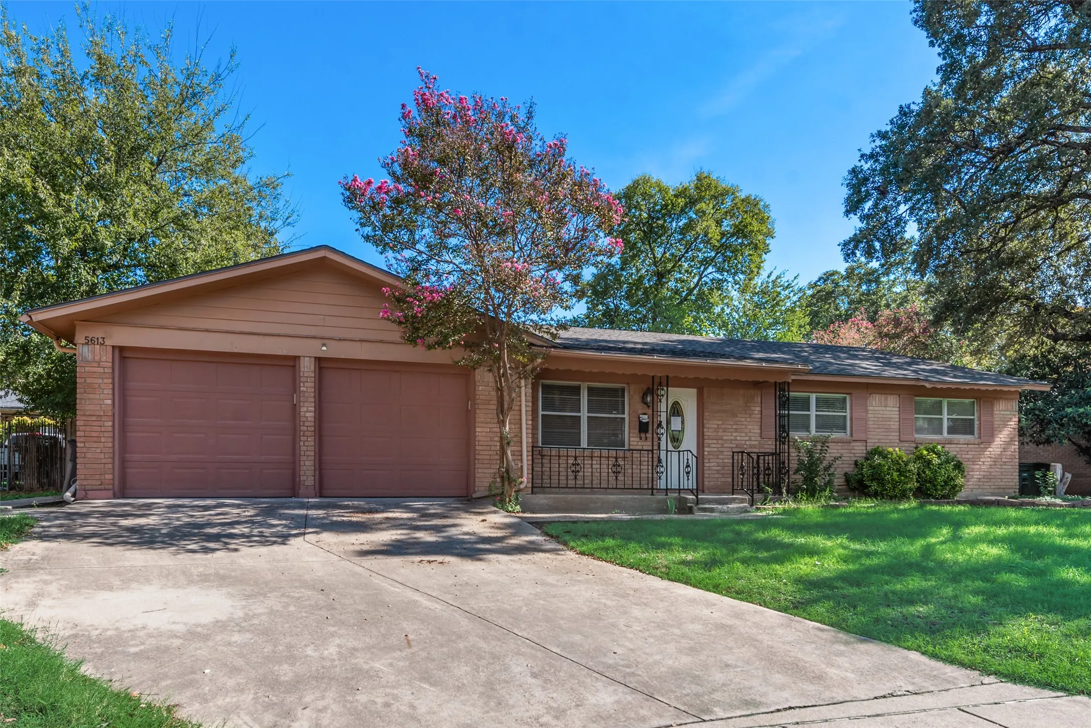 Single-story ranch-style exterior featuring brick facade, two-car attached garage, concrete driveway, and front entryway with metal railing