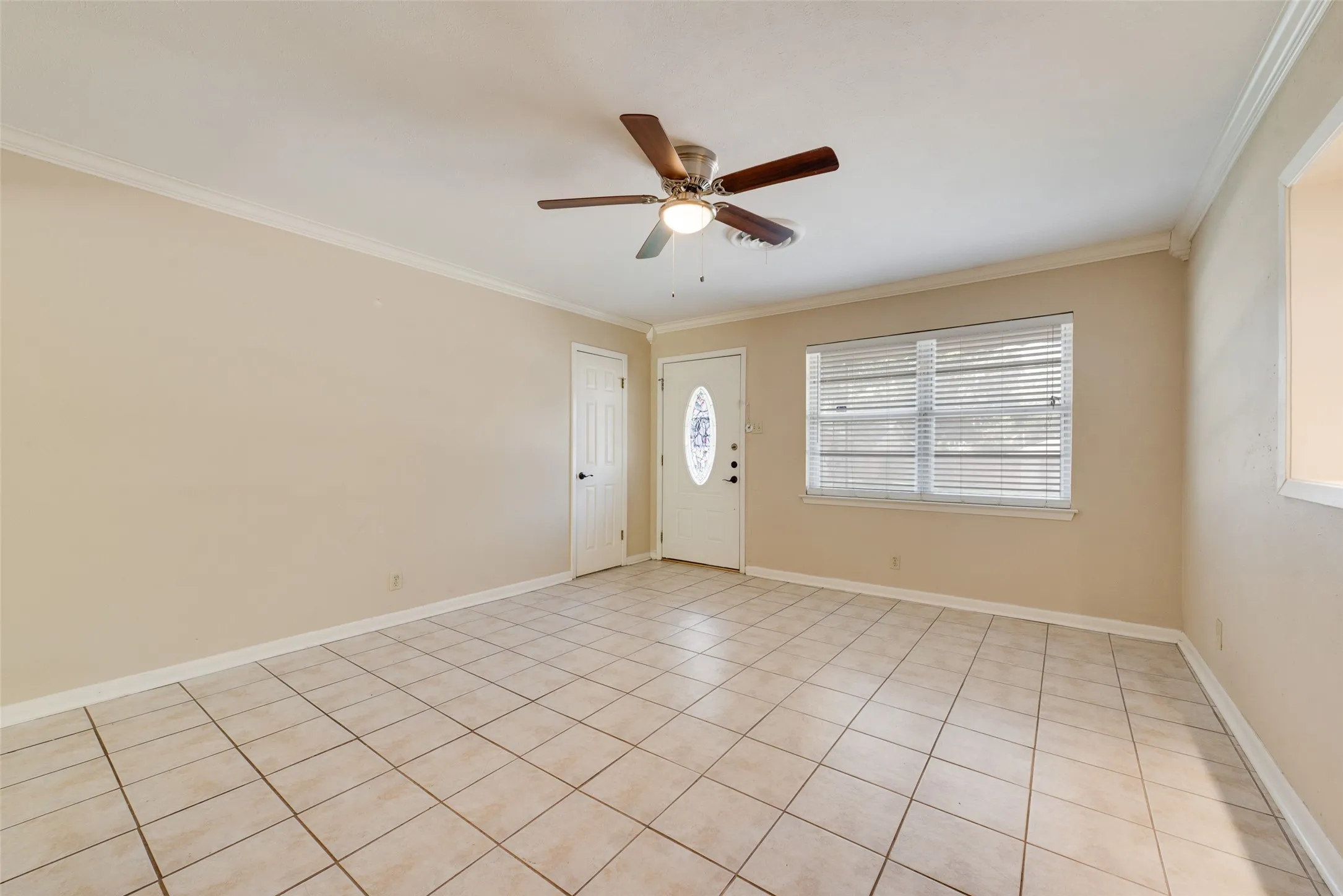 Interior space featuring ceramic tile flooring, a multi-blade ceiling fan with integrated lighting, a single-panel door with oval glass inset, and horizontal window blinds