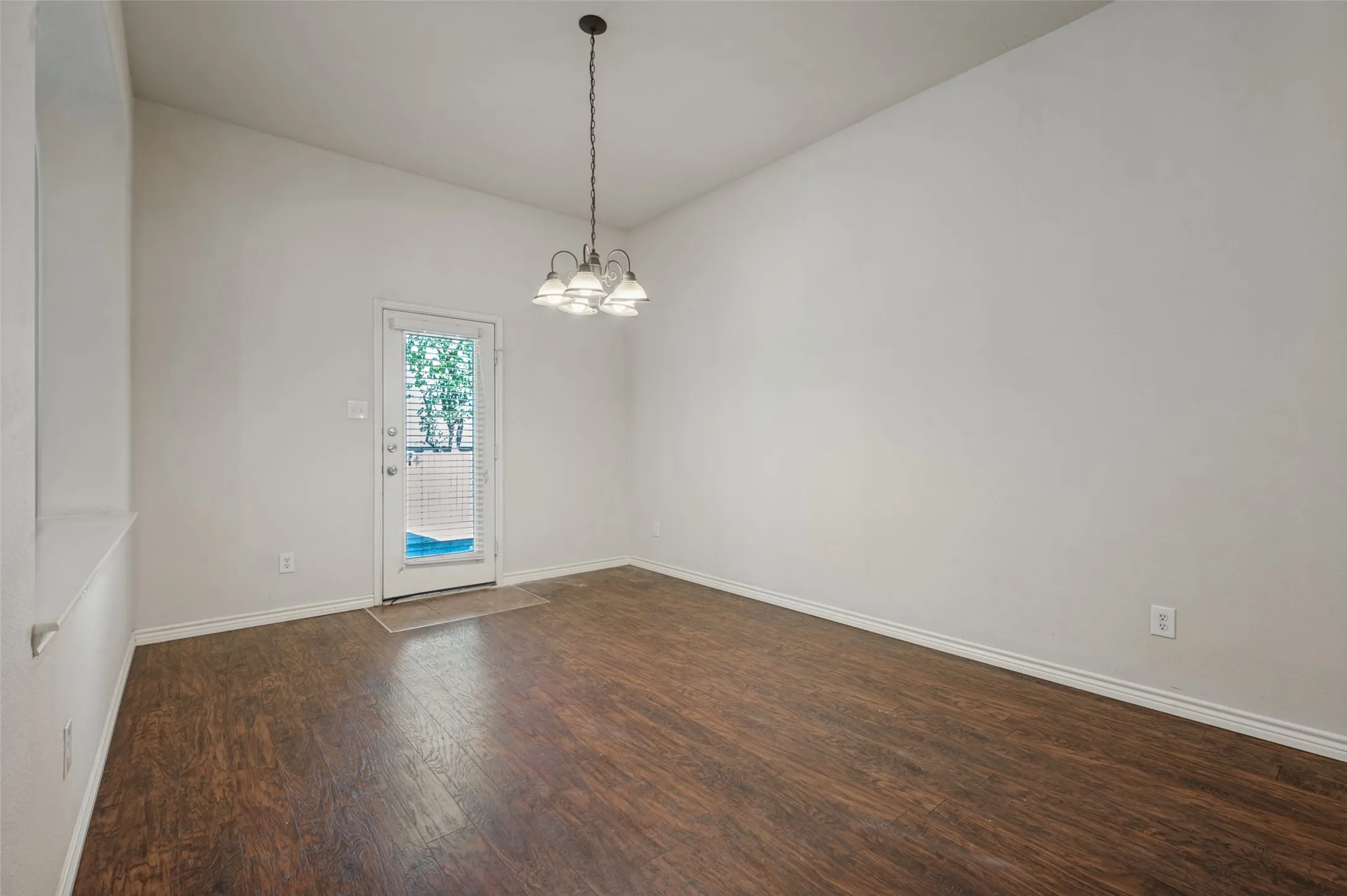 Wood-finish flooring, high ceilings, four-light pendant fixture, and glass-paneled exterior door