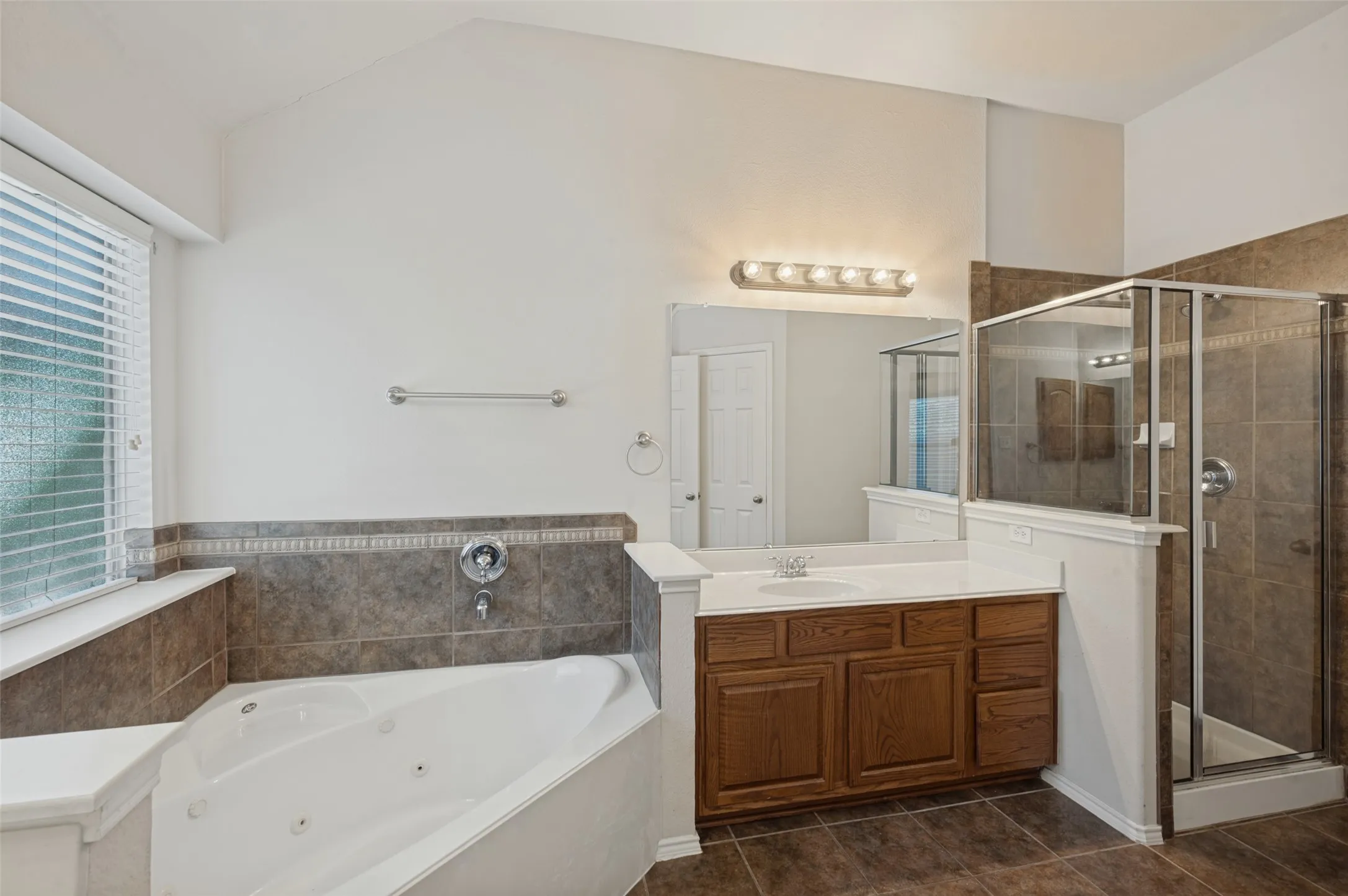 Corner jetted tub with tile surround, wood cabinetry vanity, integrated sink, and glass-enclosed shower with tile wall finish