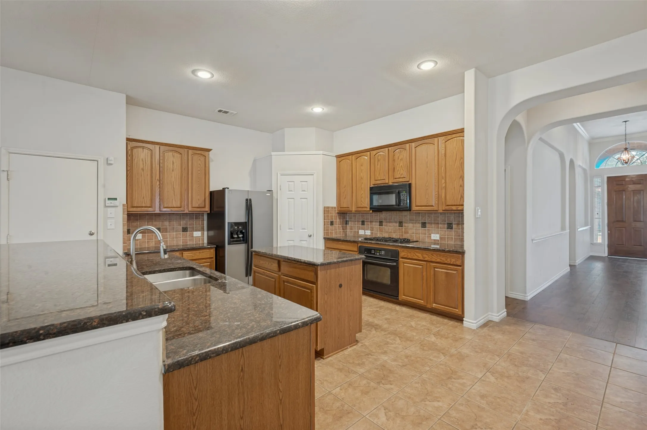 Kitchen featuring a center island, stone-finish countertops, wood-finish cabinetry, built-in black appliances, and recessed lighting