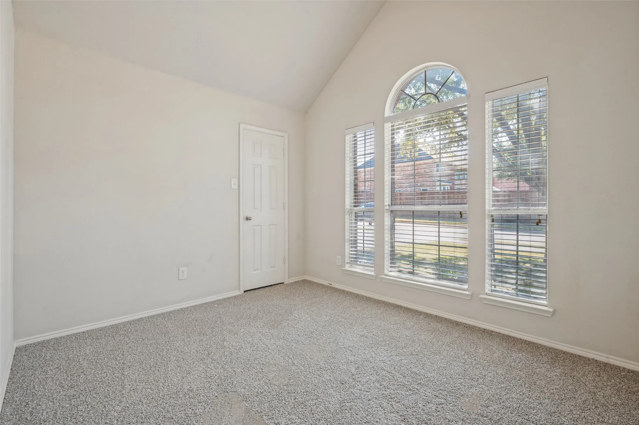 Vaulted ceilings, neutral carpeting, and a prominent arched window assembly with integrated blinds