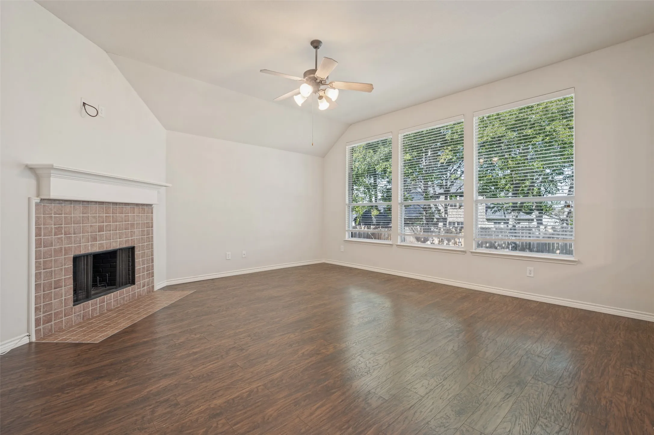 Vaulted ceilings, wood-finish flooring, fireplace with a tile surround and mantel, and large windows with integrated blinds