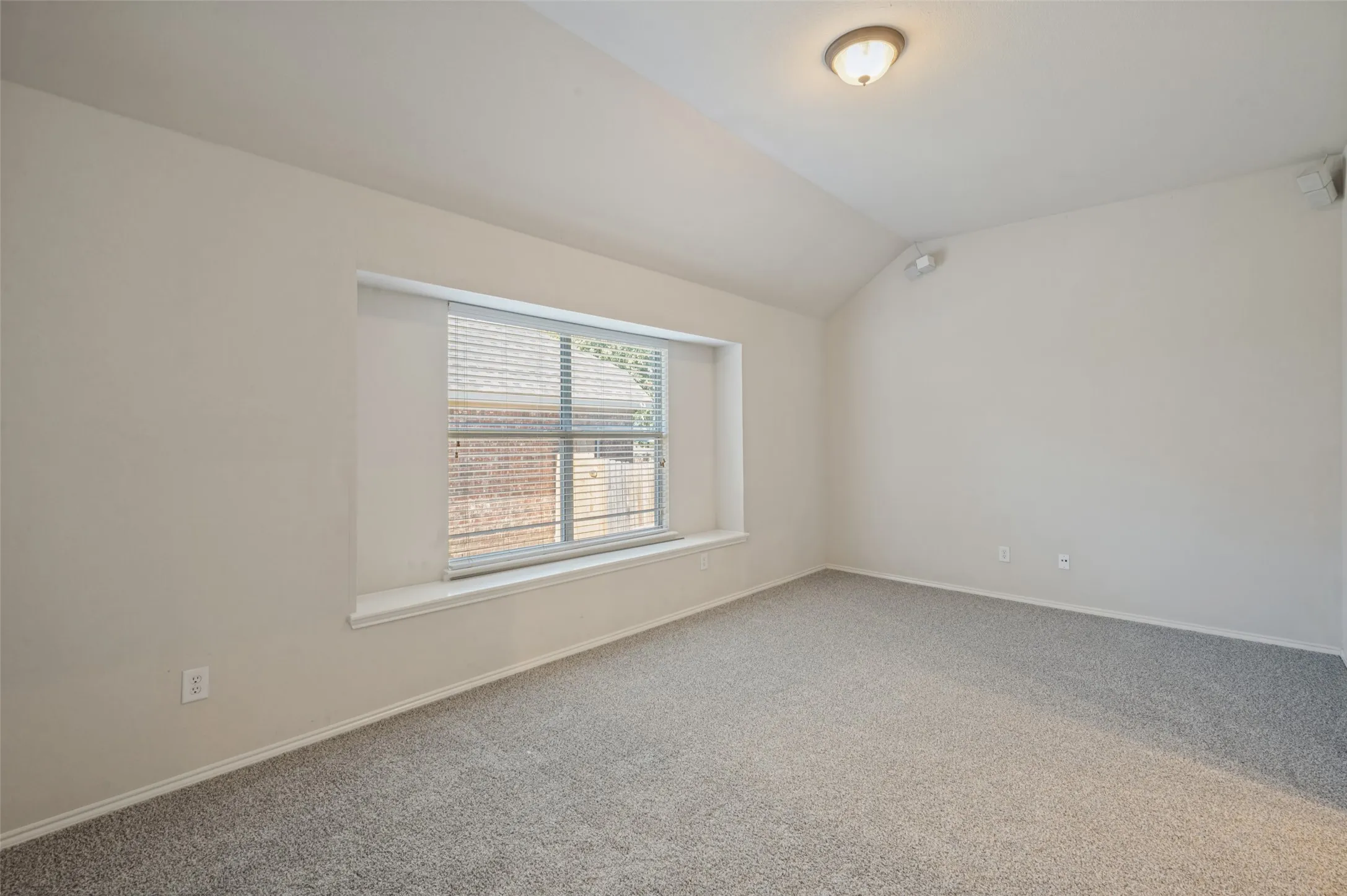 Vaulted ceilings, neutral wall color, carpeted flooring, and a recessed window with a built-in sill