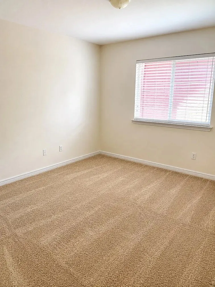 Neutral-toned interior room featuring wall-to-wall carpeting, window blinds, and a flush-mount ceiling light fixture