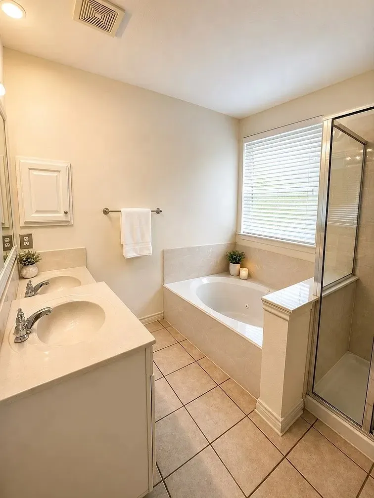 Dual-sink vanity with a solid-surface countertop, jetted soaking tub, tiled shower enclosure with a glass door, and ceramic tile flooring