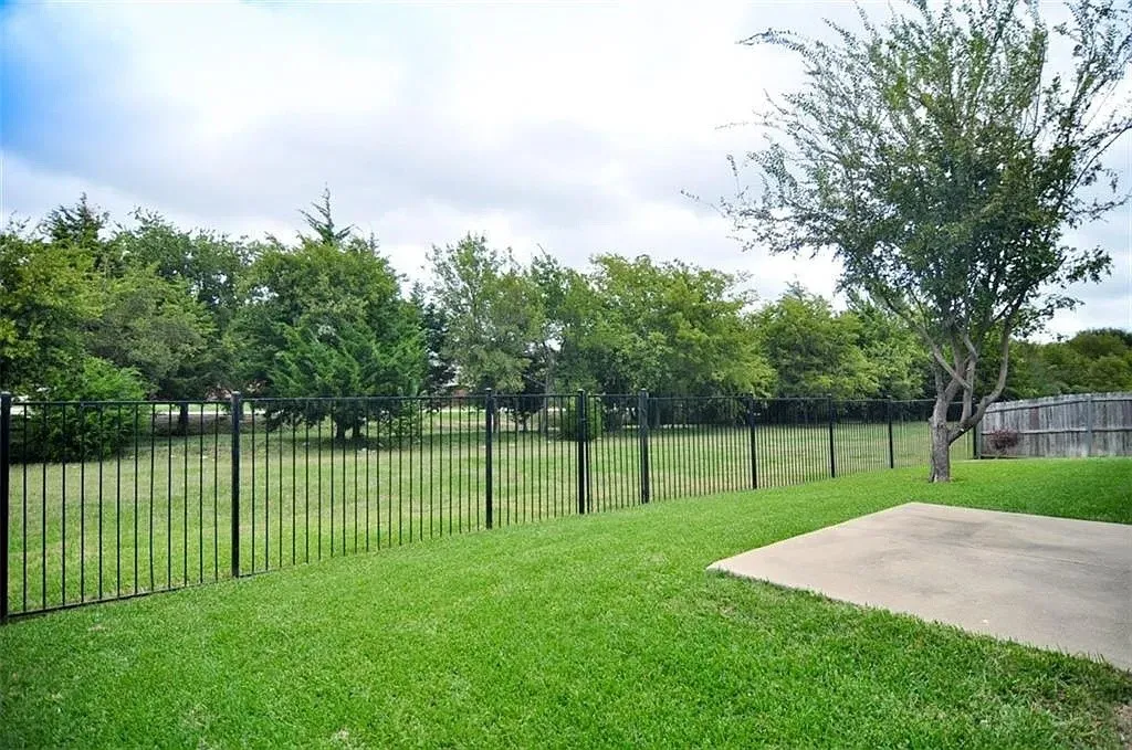 Expansive backyard featuring a level lawn, concrete patio, black metal fencing, and mature trees