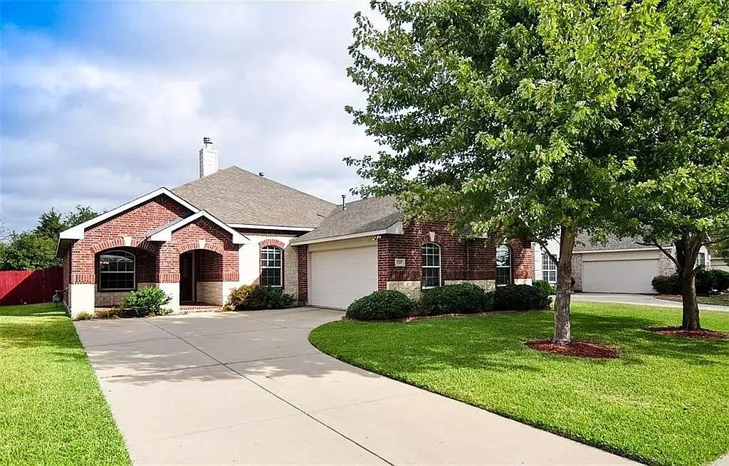 Single-story brick exterior featuring a covered entryway, attached multi-car garage, arched window accents, and a concrete driveway