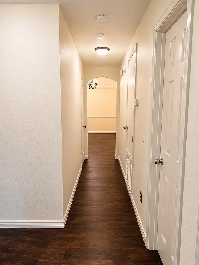Hallway featuring wood-finish flooring, white panel doors, recessed ceiling lighting, and an arched entry
