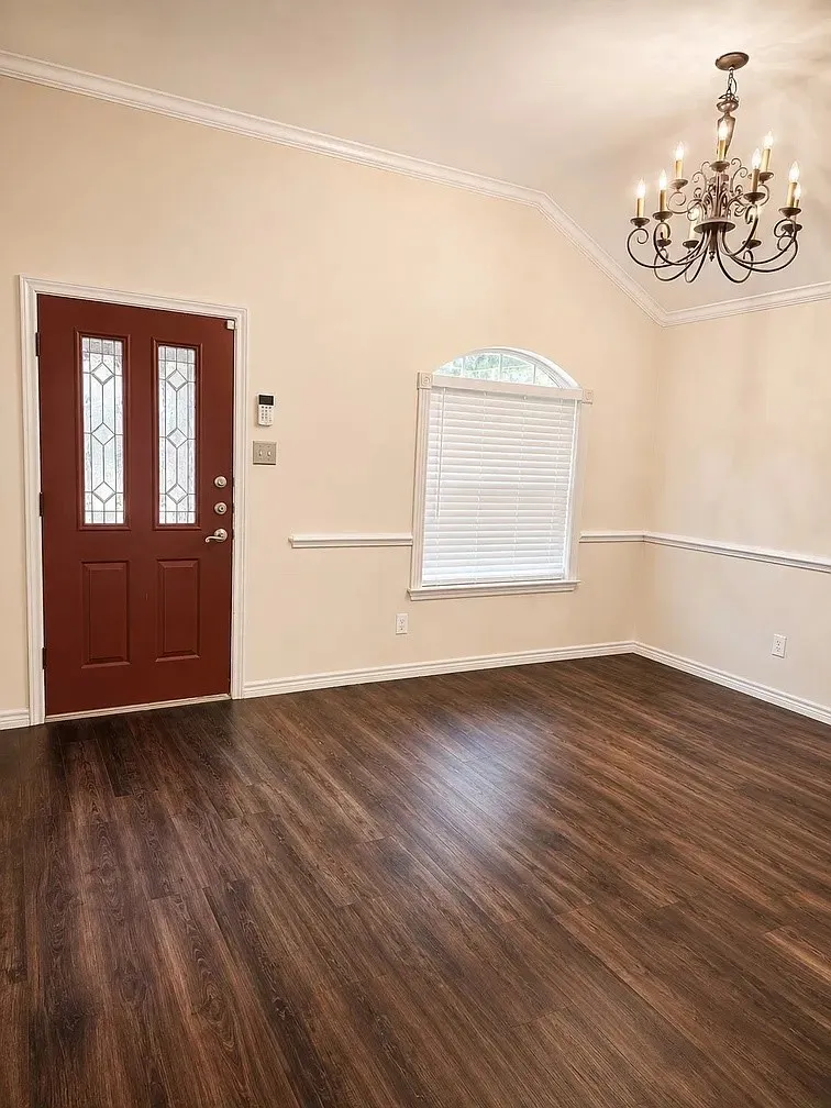 Vaulted ceiling with an arched window, wood-finish flooring, decorative chair rail molding, and a multi-arm chandelier