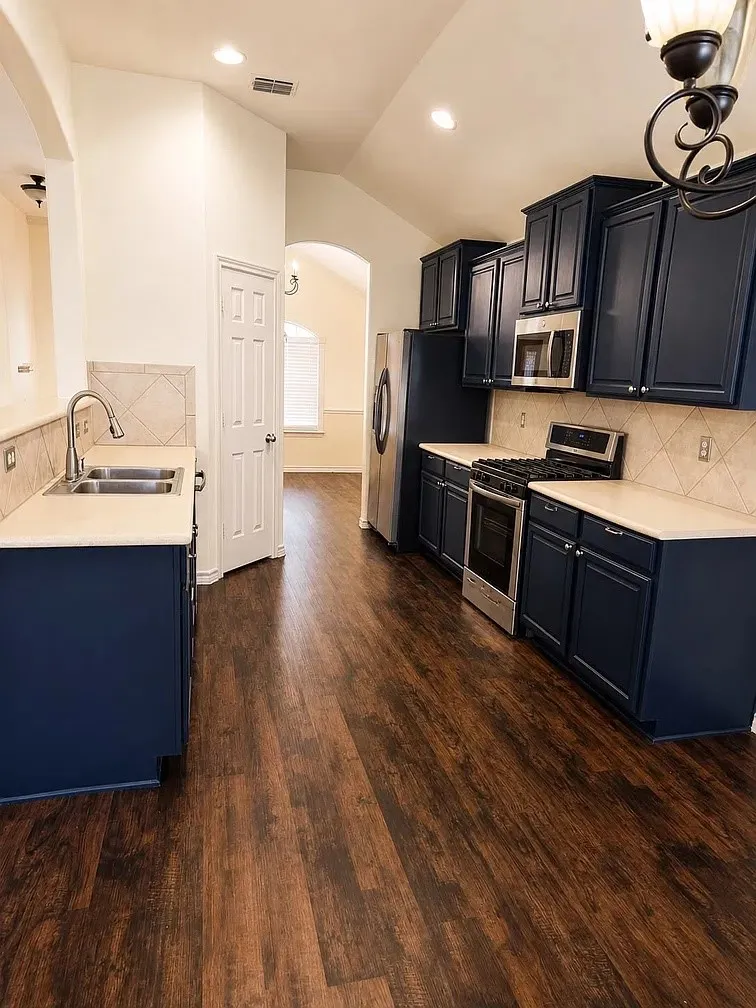Kitchen featuring dark-toned cabinetry, light-colored countertops, stainless steel appliances, tile backsplash, and wood-finish flooring