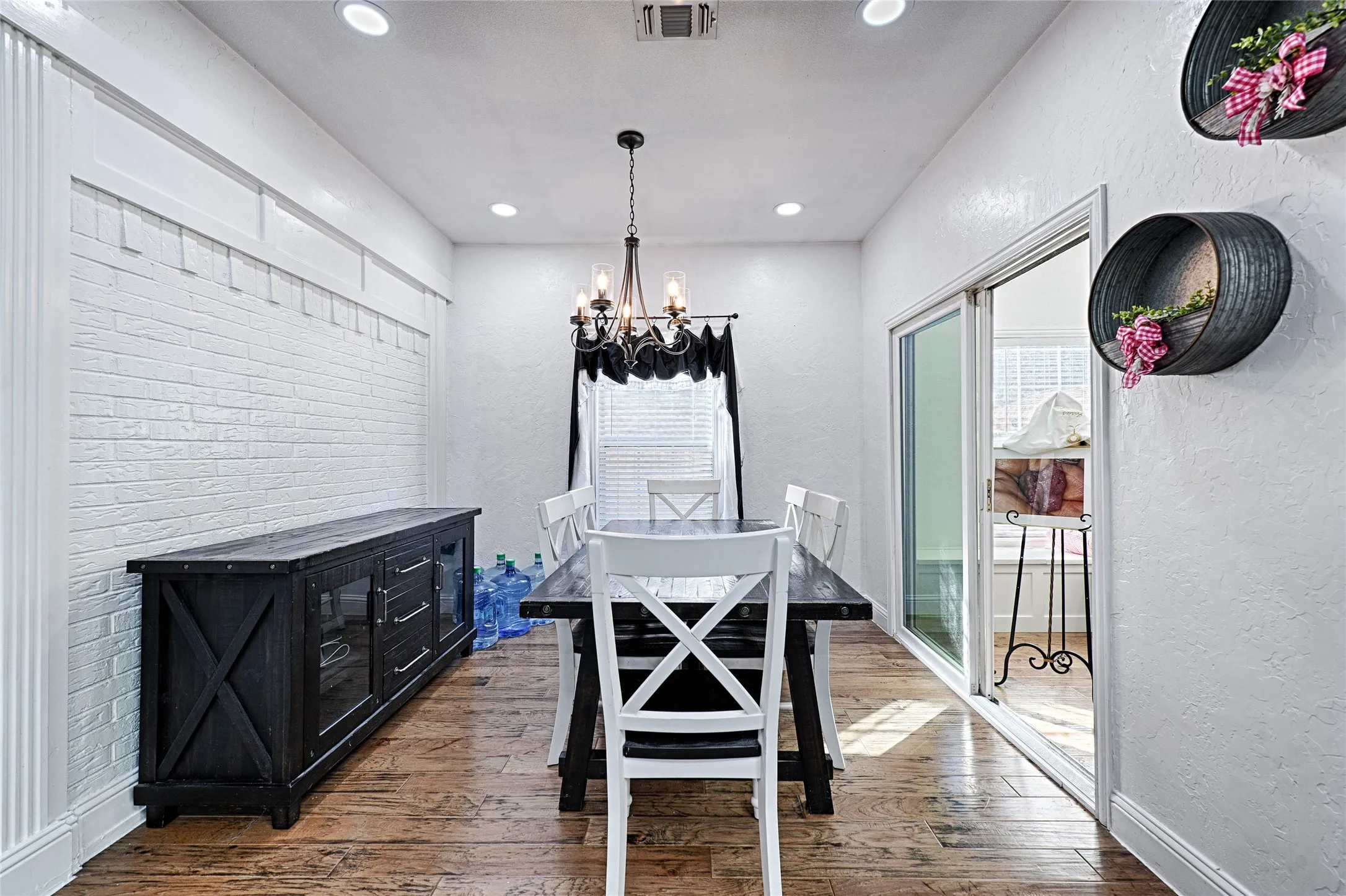 Painted brick accent wall, wood flooring, chandelier, recessed lighting, and sliding glass doors providing natural light.