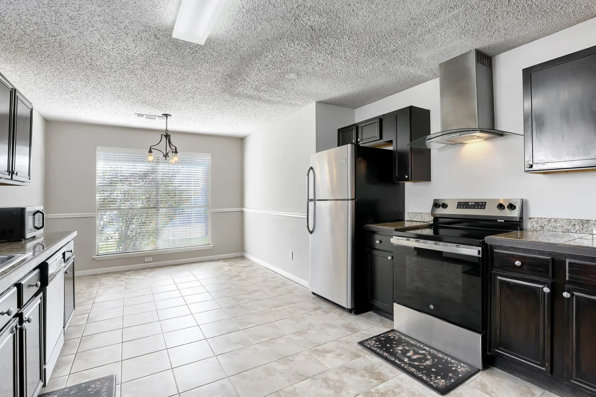 Kitchen featuring dark cabinetry, stone-finish countertops, a stainless steel range with a glass-canopy vent hood, and tile flooring