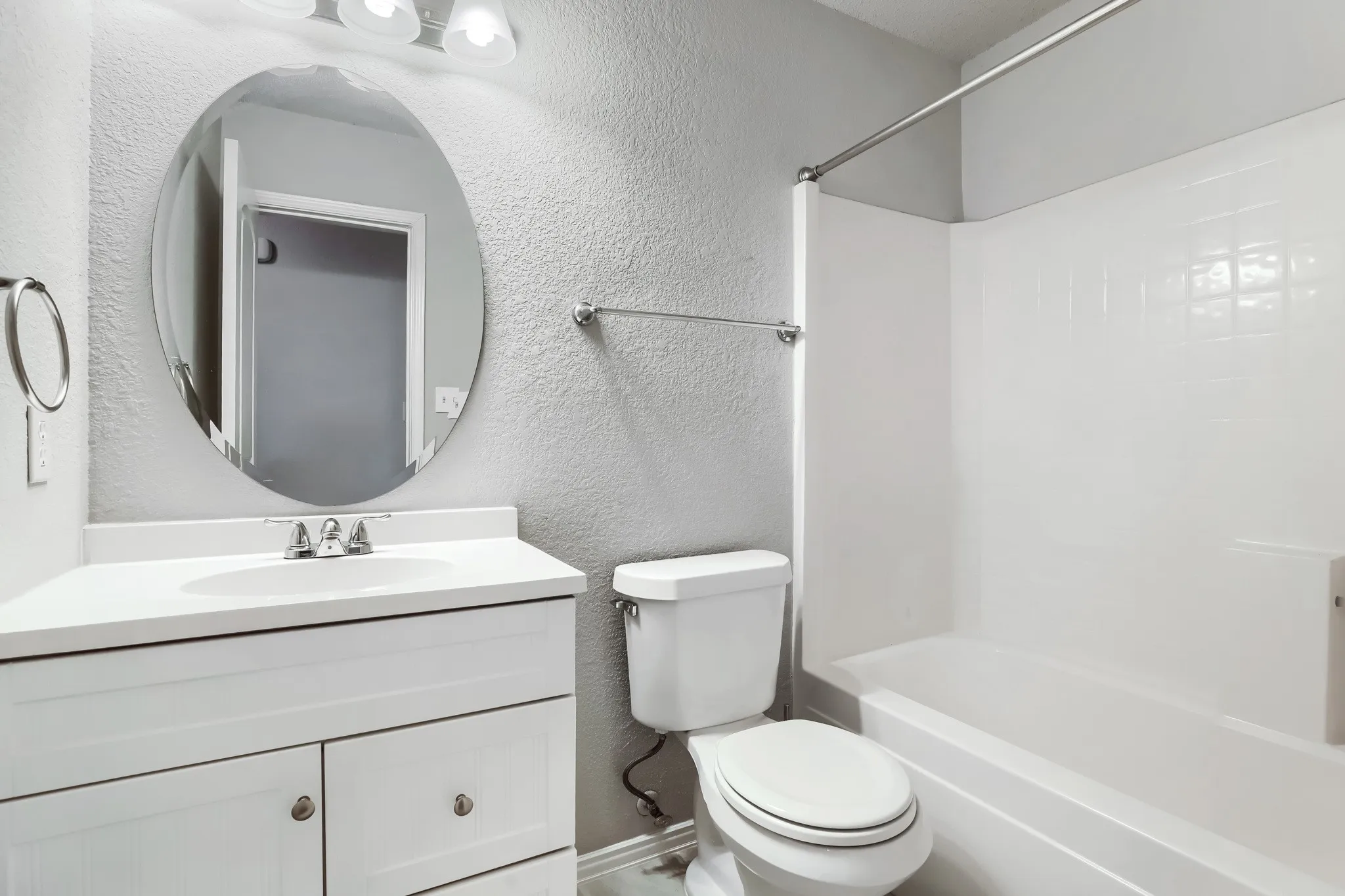 Bathroom featuring a white vanity with an integrated sink, oval wall-mounted mirror, three-light fixture, and a white tiled shower-tub combination