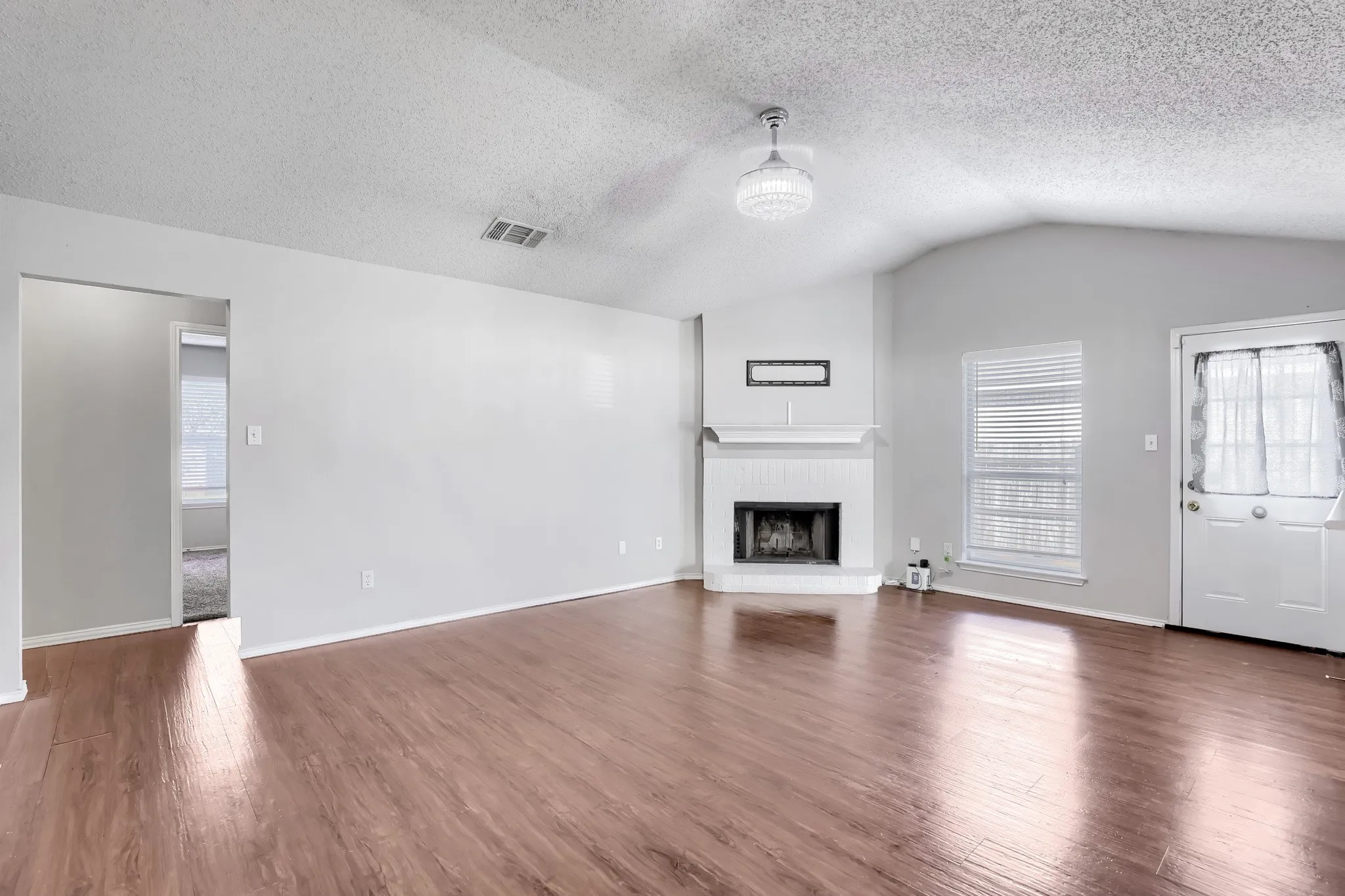 Vaulted ceilings, wood-finish flooring, corner fireplace with white hearth, and integrated globe lighting