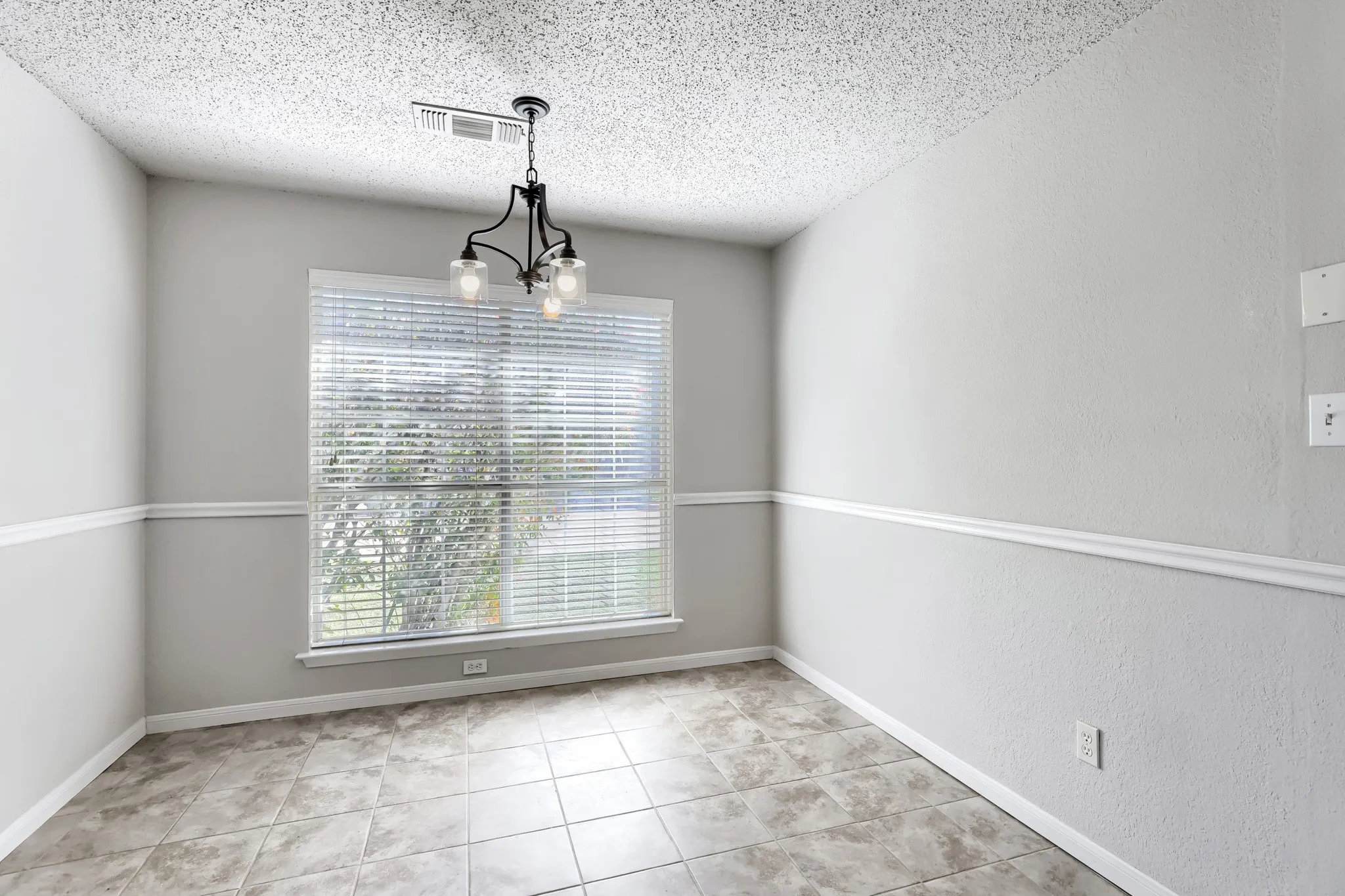 Neutral-toned interior space featuring light-colored tile flooring, chair rail molding, and a metal multi-light chandelier
