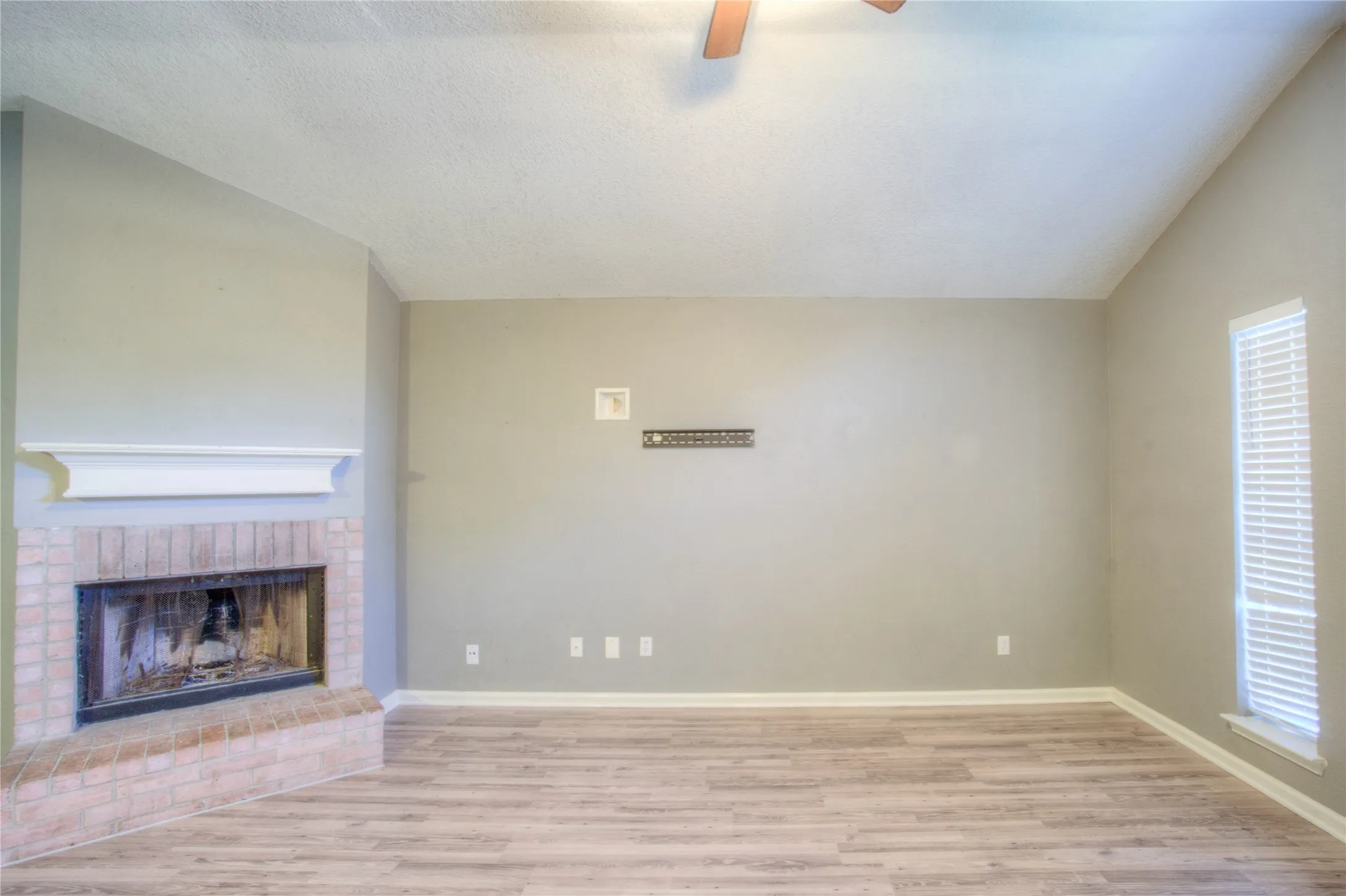 Vaulted ceilings featuring a ceiling fan, wood-finish flooring, and a brick fireplace with a prominent mantle