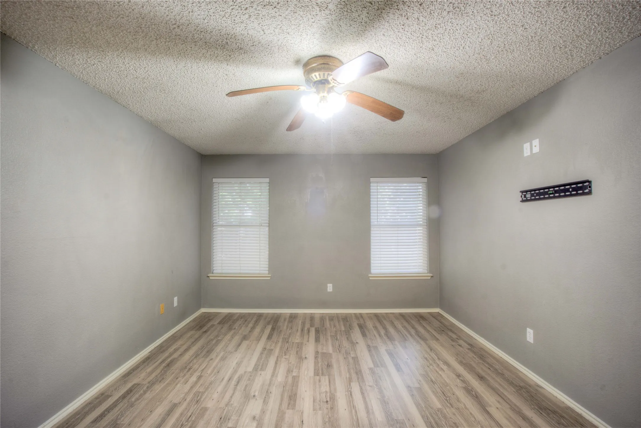 Room featuring wood-finish flooring, dual windows with fitted blinds, and a central ceiling fan with integrated lighting