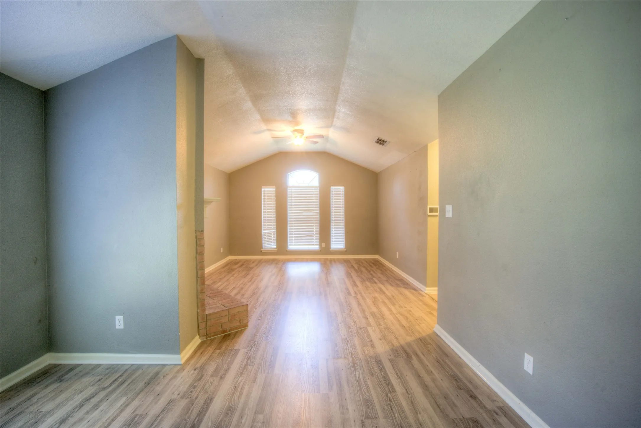 Vaulted ceiling featuring an integrated fan, wood-finish flooring, and a stone-accented fireplace hearth