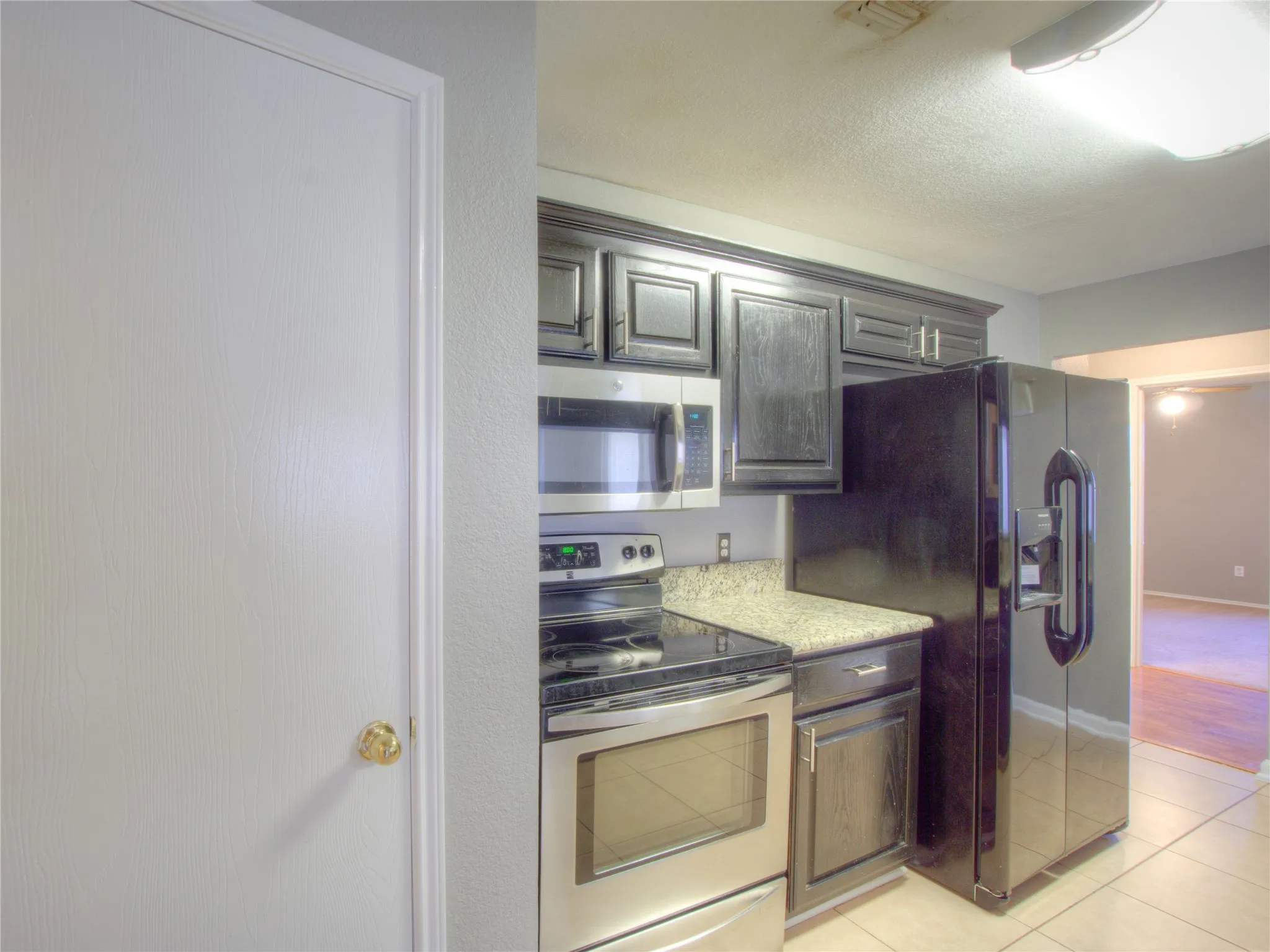 Kitchen featuring dark wood-finish cabinetry, stone-style countertops, stainless steel appliances, and tile flooring