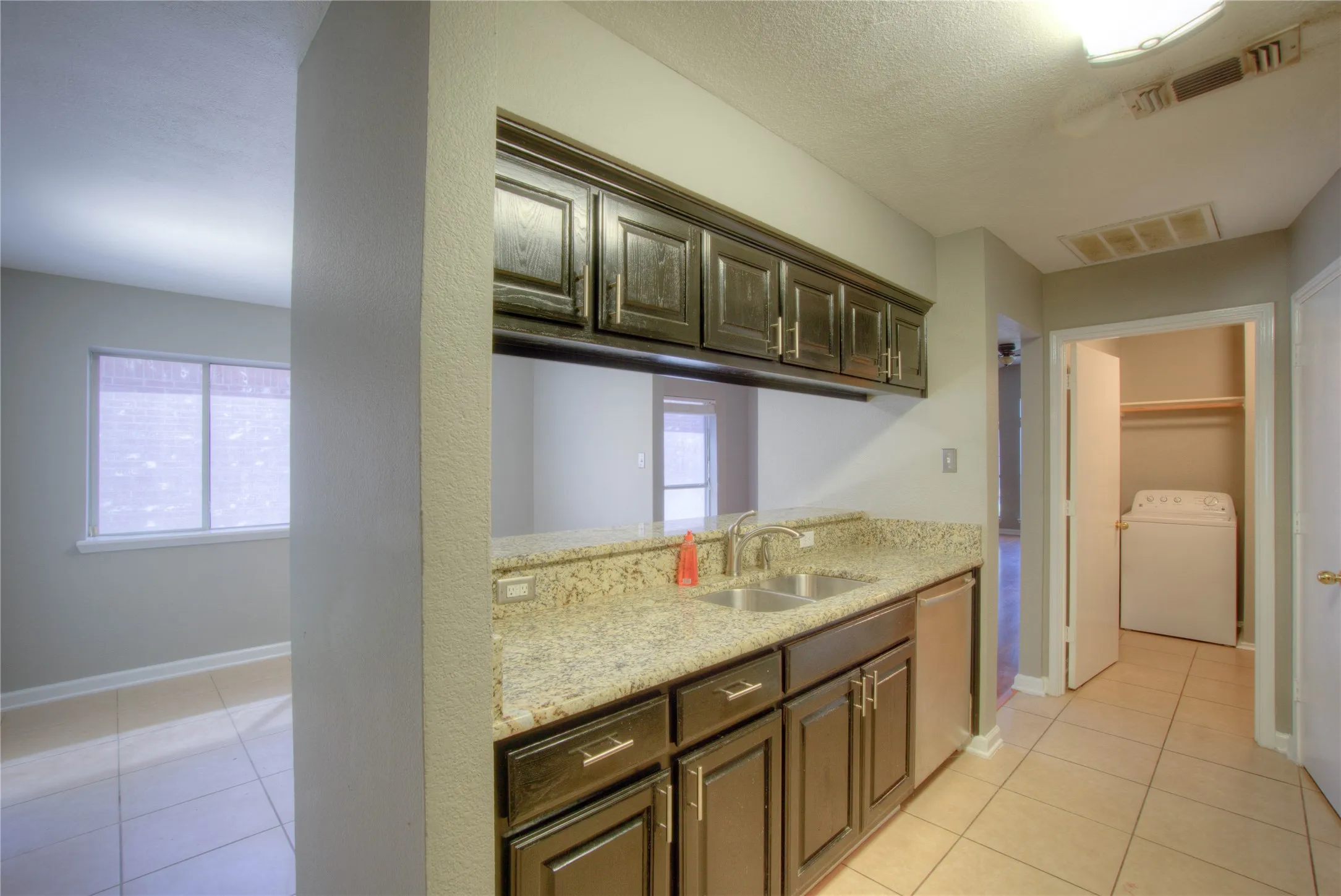 Dark wood-finish cabinetry, stone-texture countertops, undermount double-basin stainless steel sink with gooseneck faucet, tile flooring, and integrated dishwasher