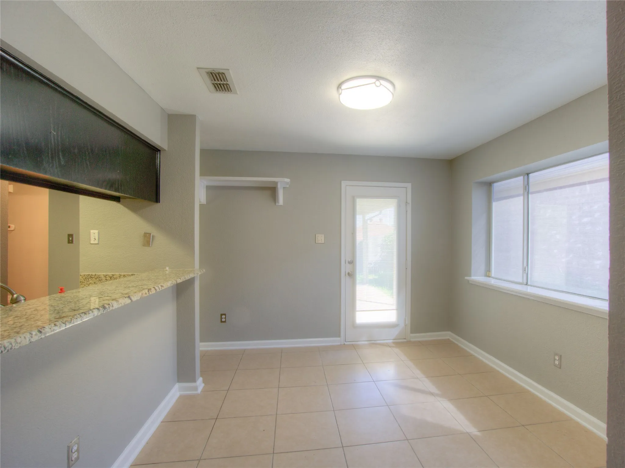 Stone-surfaced breakfast bar with integrated pass-through, neutral tile flooring, multi-pane glass door, and large window with sill