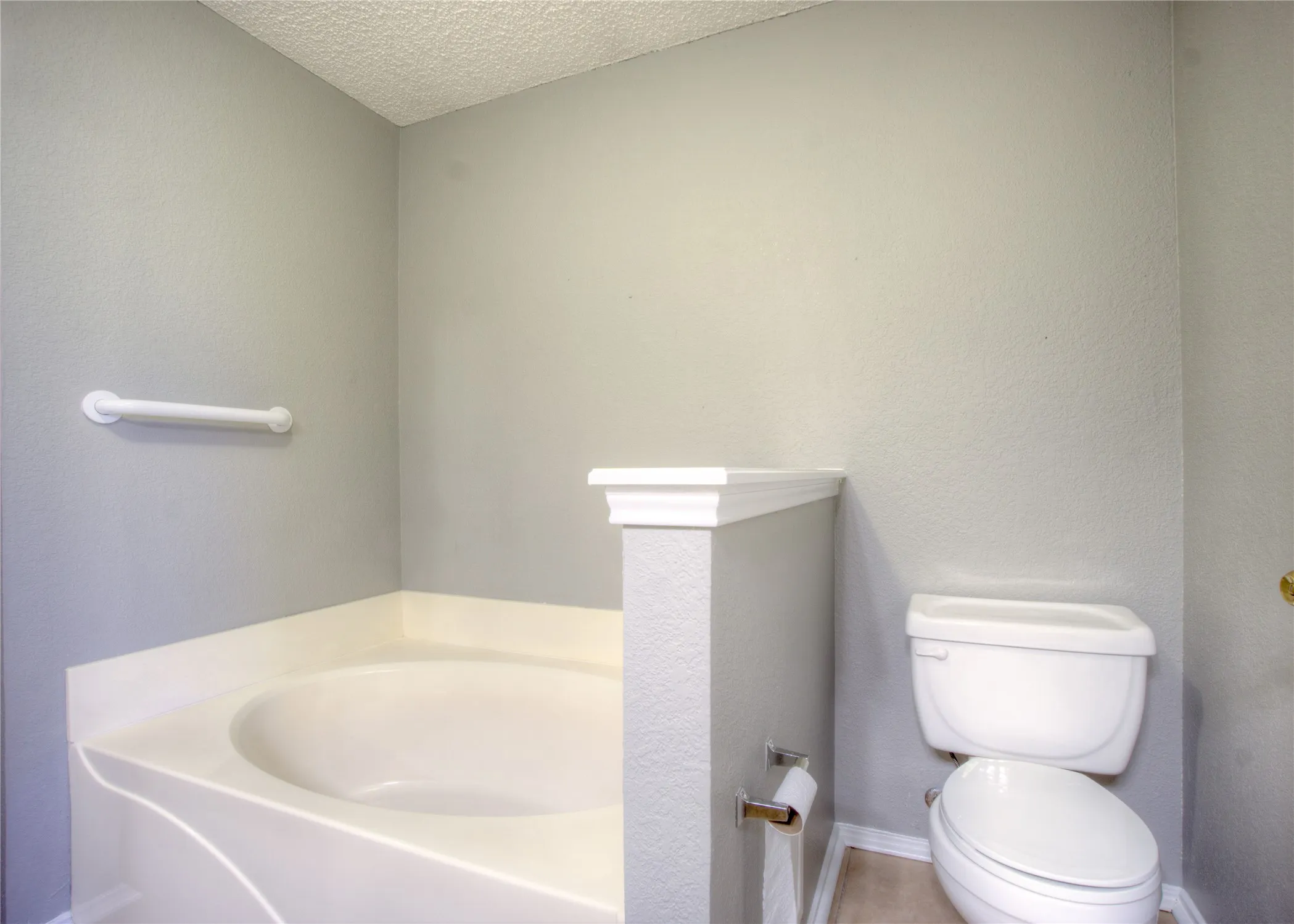 Built-in soaking tub with a low-profile surround, white porcelain toilet, and wall-mounted grab bar