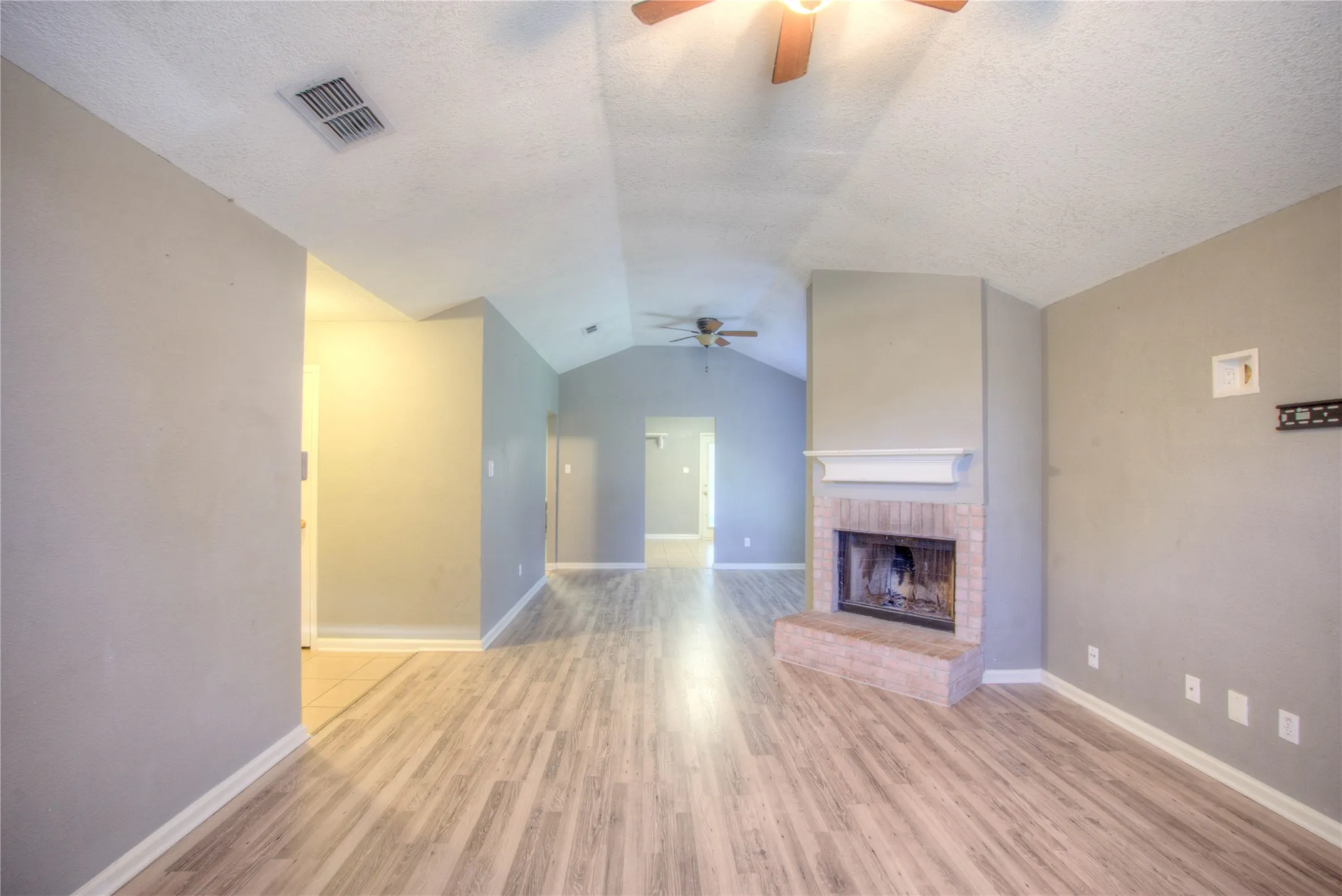 Vaulted ceilings, wood-finish flooring, masonry fireplace with a white mantel, and ceiling fans