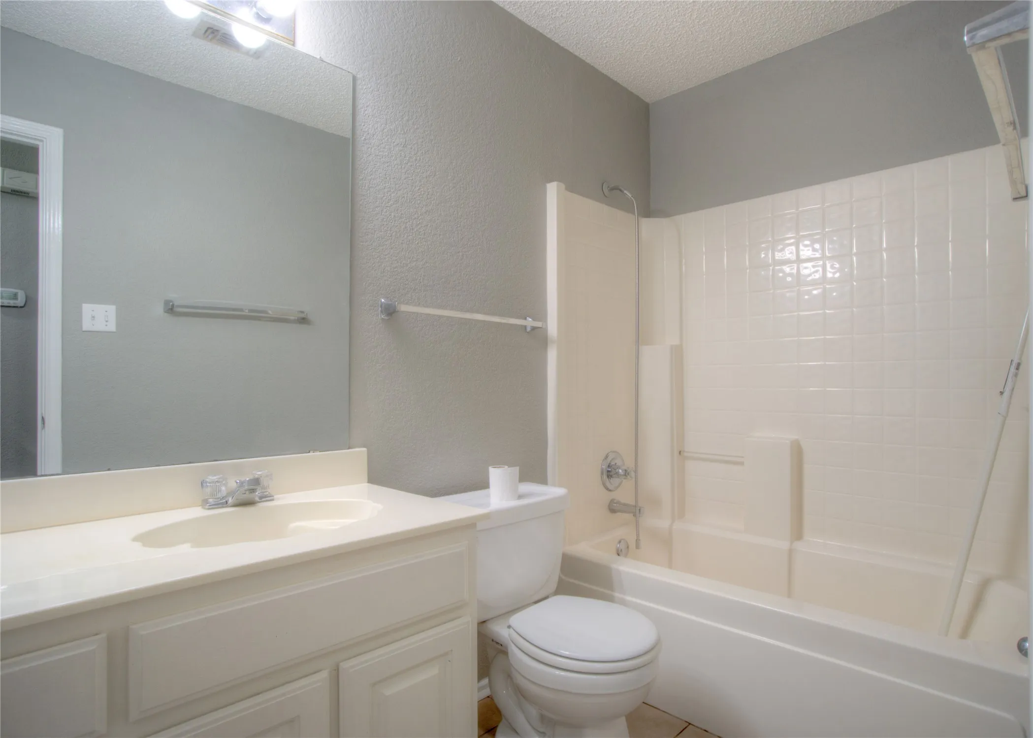 Full-width vanity with an integrated sink, polished chrome faucet, expansive wall-mounted mirror, and a tub-shower combination with tiled surround