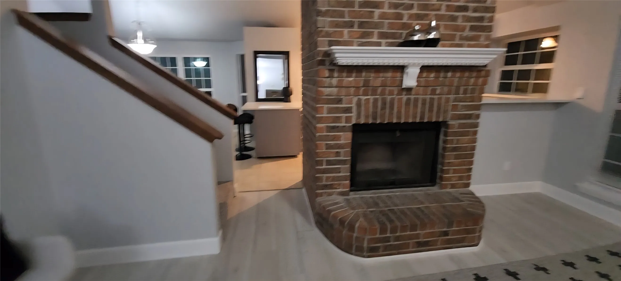 Floor-to-ceiling brick fireplace with a decorative mantel, wood-finish flooring, and staircase with a wooden handrail