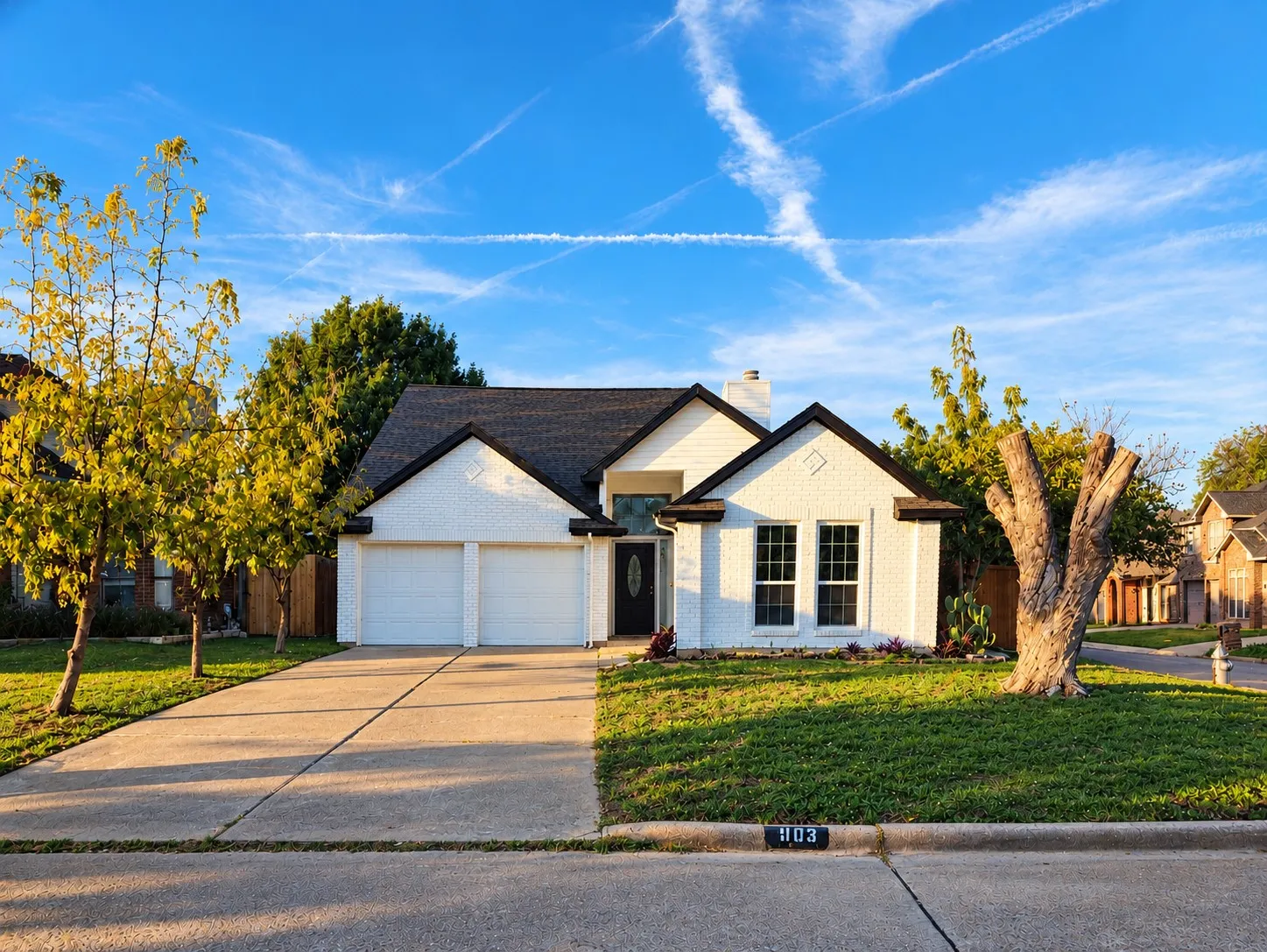 Single-story exterior featuring painted brick masonry, a gabled roofline, a two-car garage, and a concrete driveway