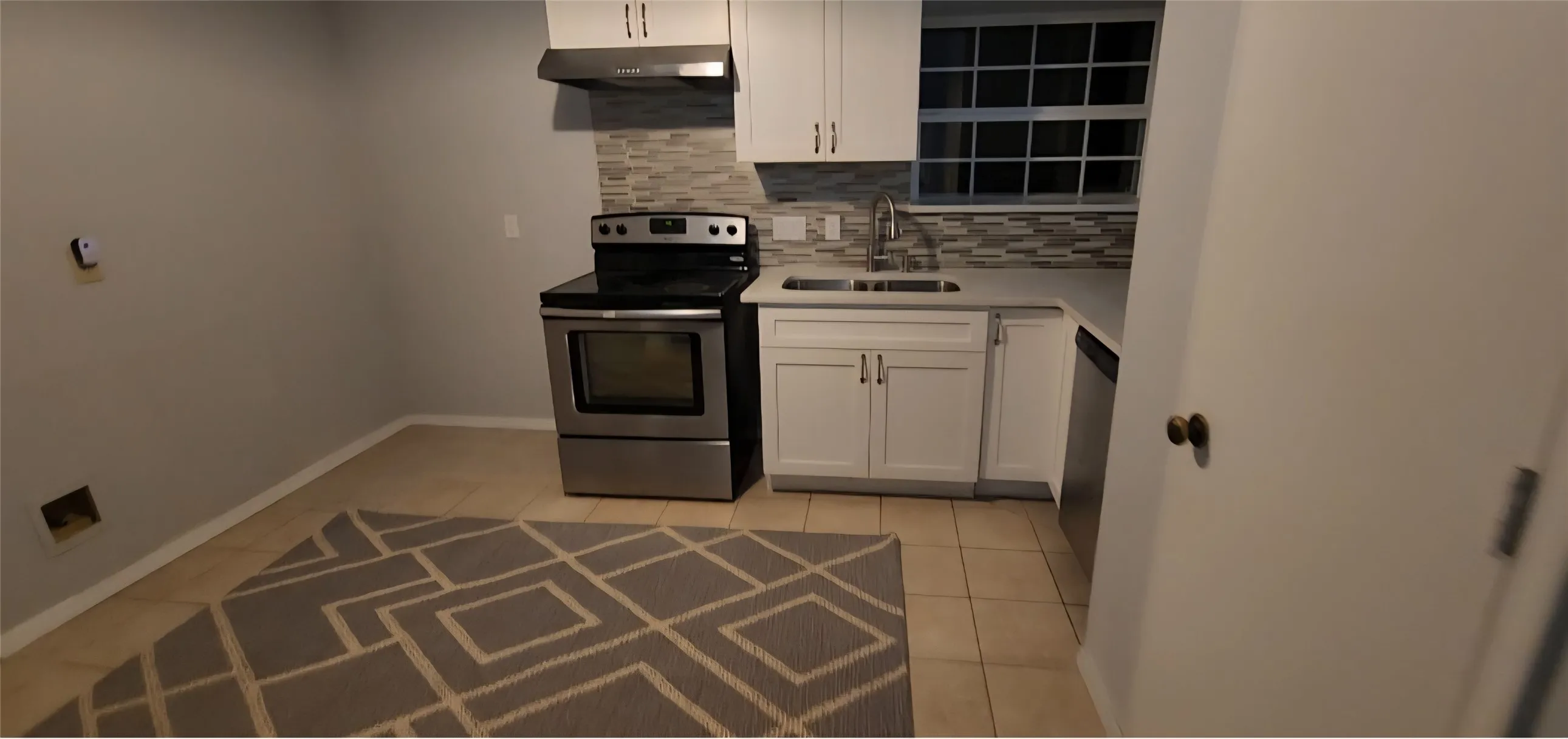Kitchen featuring white shaker-style cabinetry, stainless steel appliances, multi-tonal mosaic tile backsplash, double-basin sink, and tile flooring