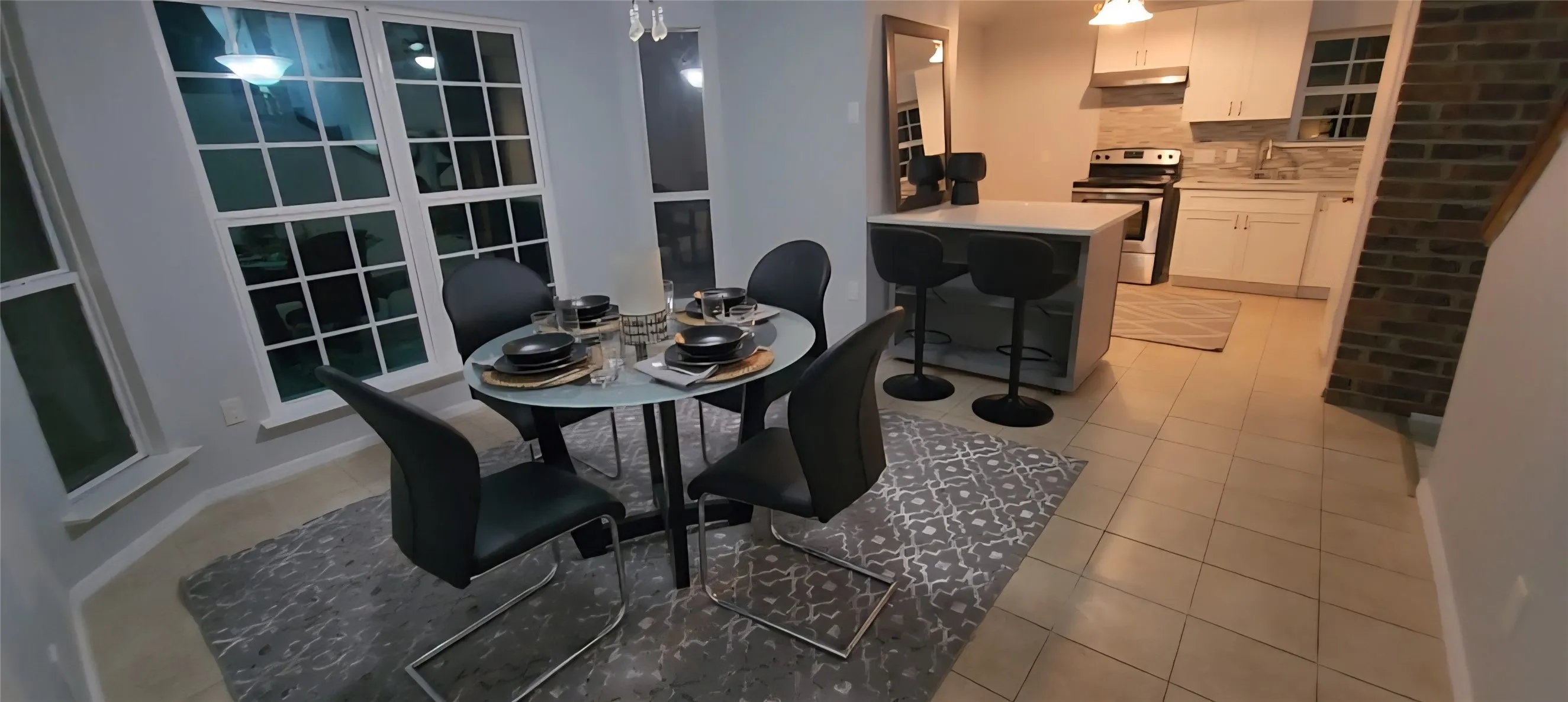 Kitchen featuring white cabinetry, a center island with counter seating, a tiled backsplash, and tile flooring, complemented by an interior brick accent wall
