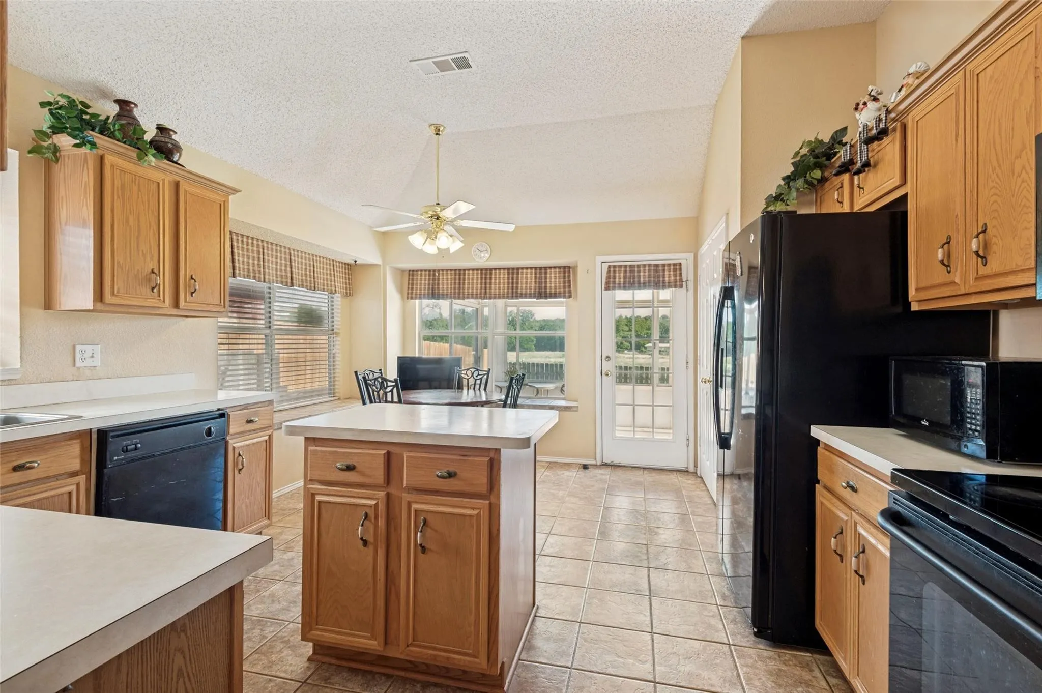 Kitchen featuring oak cabinetry, a central prep island, tile flooring, vaulted ceilings, and a light-filled breakfast nook