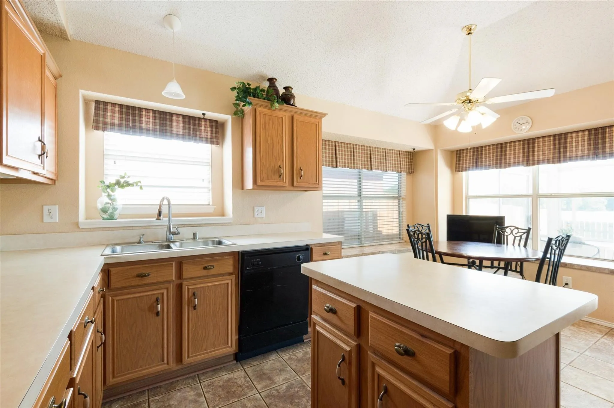 Kitchen featuring wood cabinetry, a central island with countertop, tile flooring, stainless steel sink with a gooseneck faucet, and a vaulted ceiling
