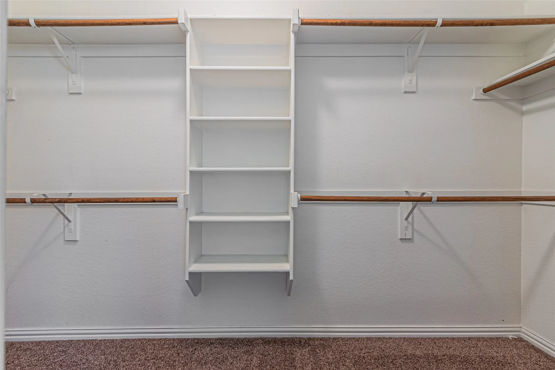 Walk-in closet featuring white built-in shelving, dual-tier wood hanging rods, and carpeted flooring