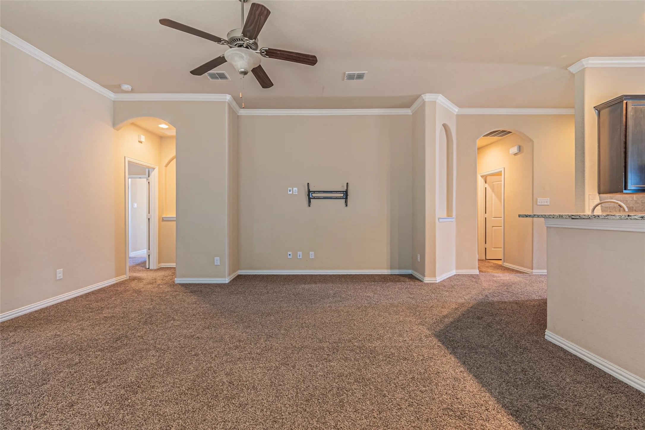 Open interior featuring crown molding, arched entryways, neutral carpeting, a ceiling fan, and a kitchen peninsula with stone countertops