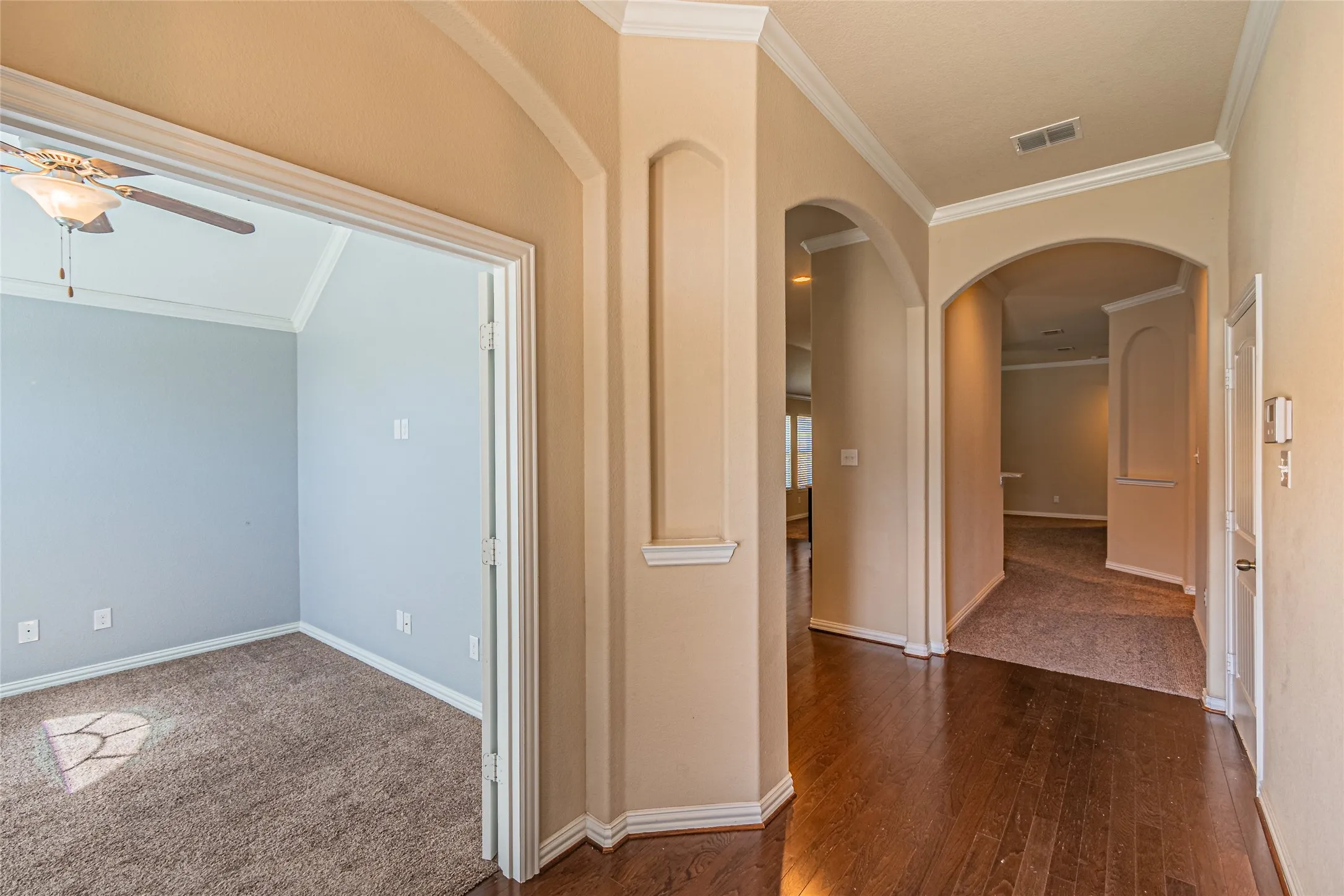 Interior hallway featuring wood-finish flooring, recessed wall niches, arched architectural entryways, crown molding, and ceiling-mounted lighting