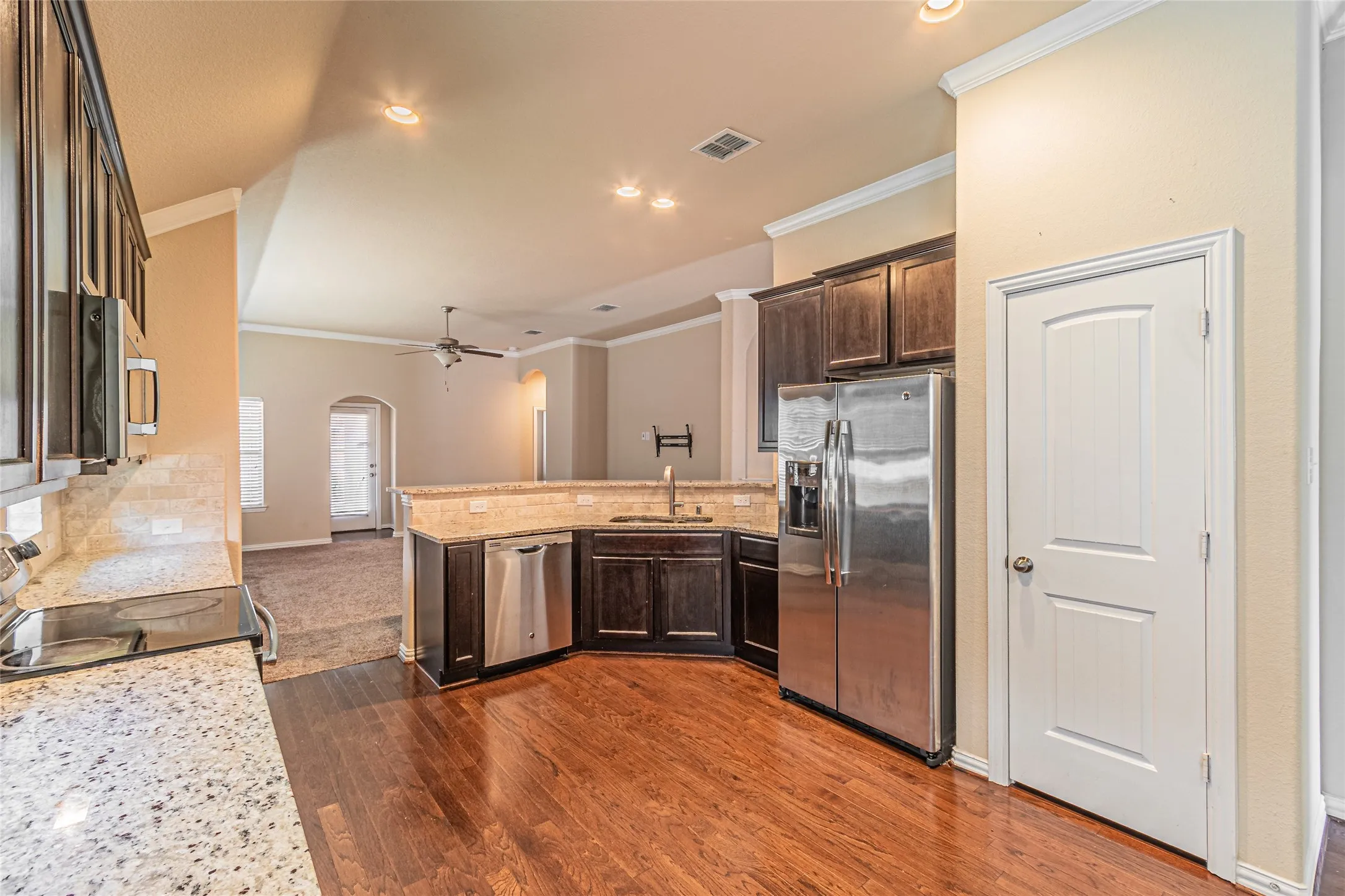 Kitchen featuring wood-finish flooring, dark-toned cabinetry, stainless steel appliances, stone-finish countertops, and recessed lighting