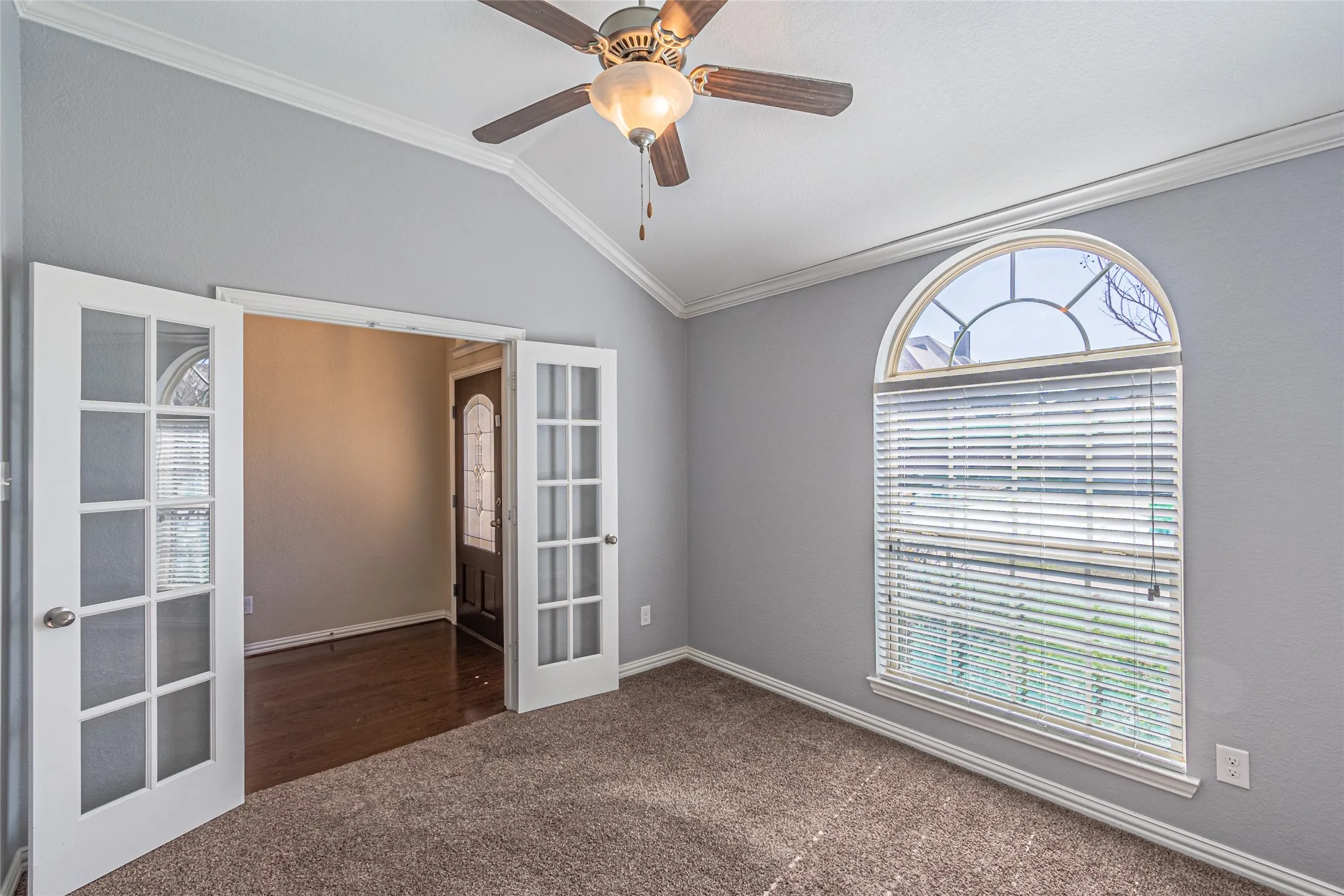 Vaulted ceiling, arched window with muntin detailing, and double French doors featuring glass panes