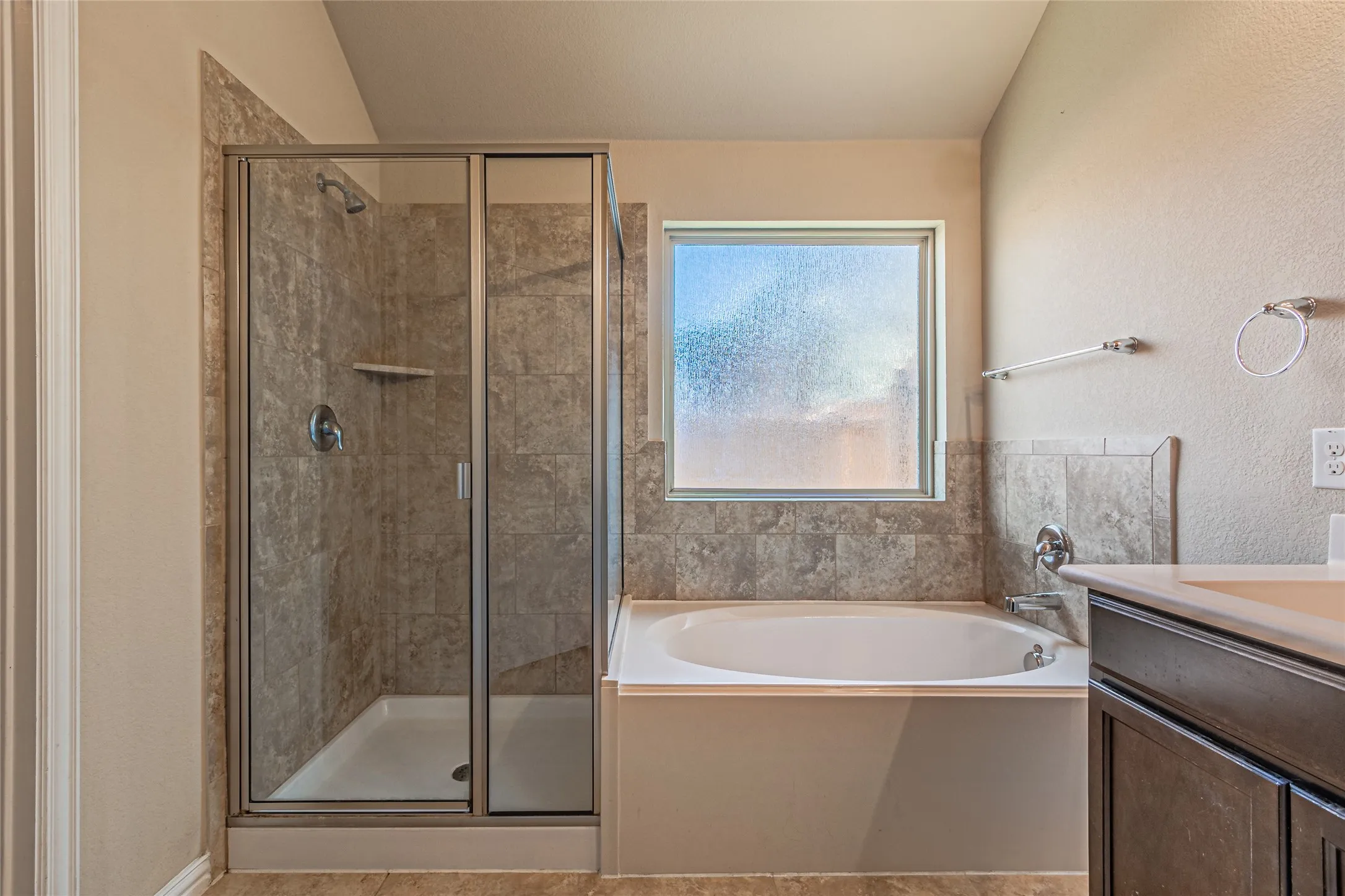 Separate shower with tile surround, deep soaking tub, tile backsplash, and dark wood-finish cabinetry with a neutral countertop