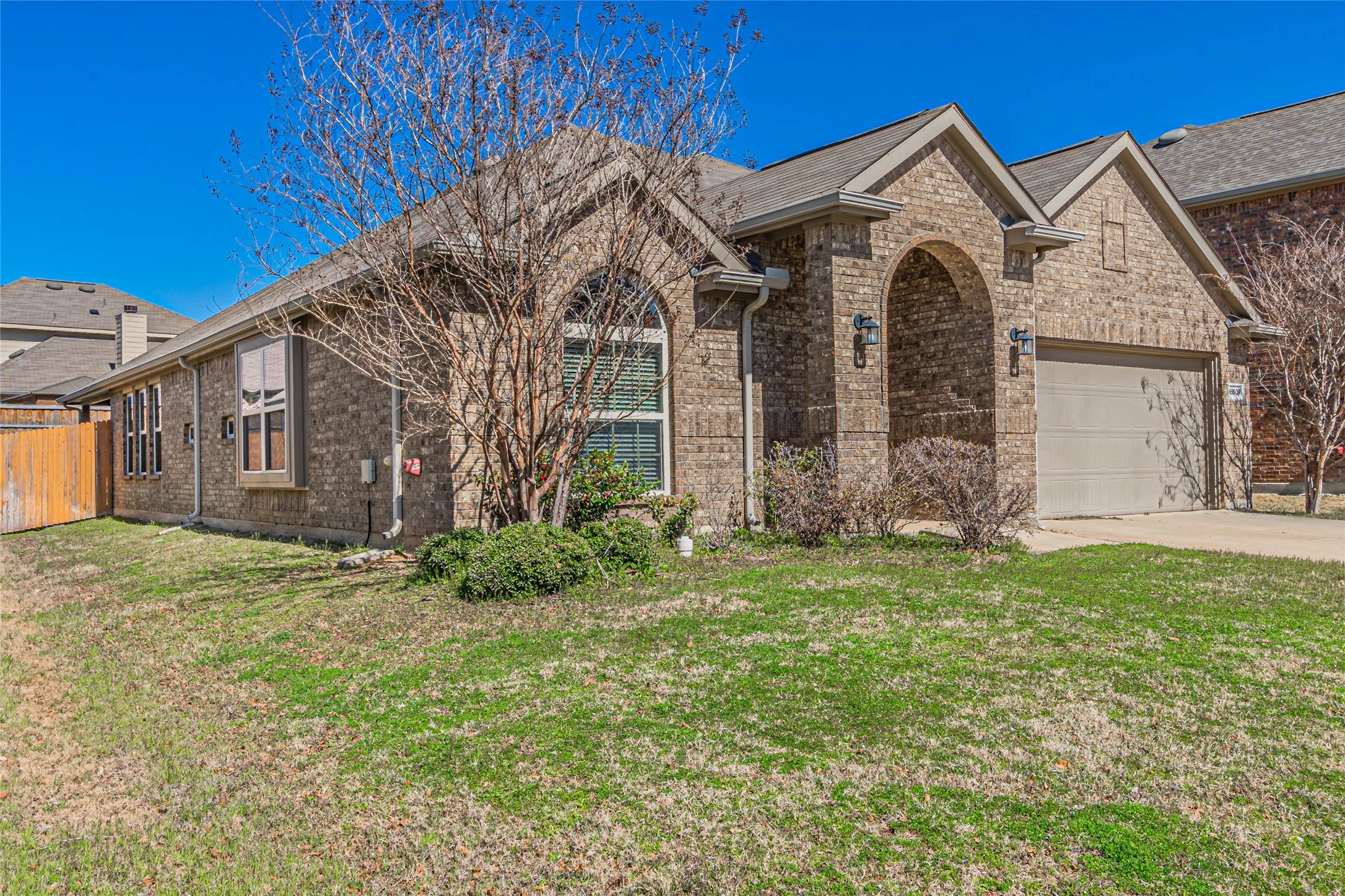 Single-story brick exterior featuring a prominent arched entryway, multiple gables, and an attached two-car garage