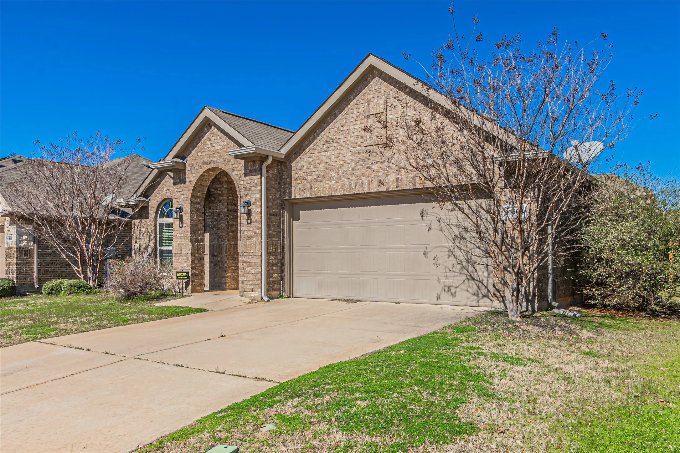Single-story brick exterior featuring a multi-gabled roofline, an arched entryway, and a double-car garage with a concrete driveway
