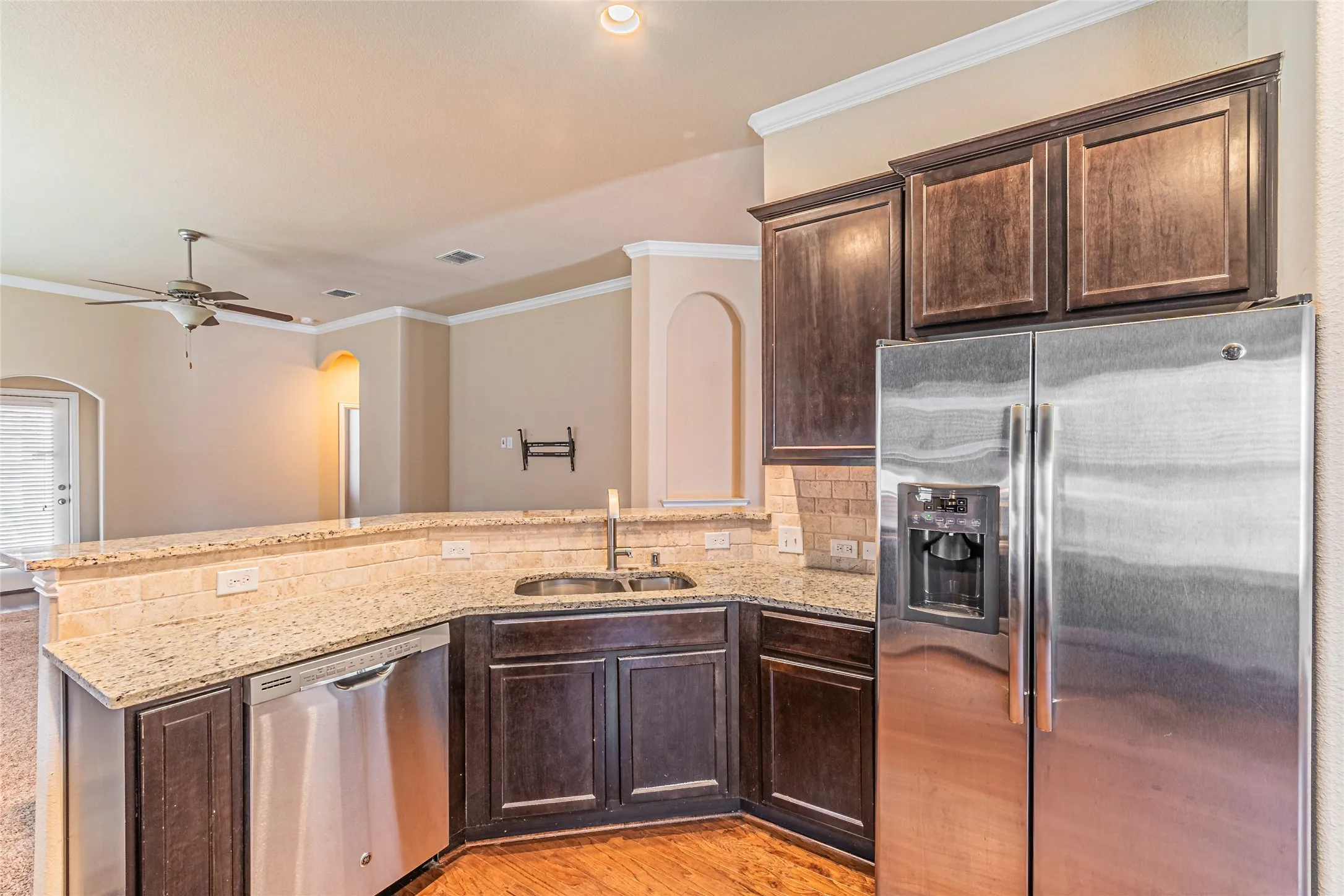 Kitchen featuring dark wood cabinetry, light-toned stone countertops, stainless steel appliances, and a double-basin undermount sink with a high-arch faucet