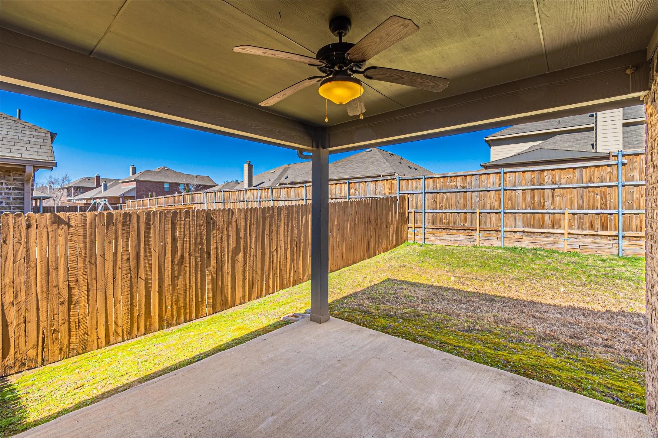Covered concrete patio featuring a ceiling fan with integrated lighting, enclosed by a full-perimeter wood privacy fence