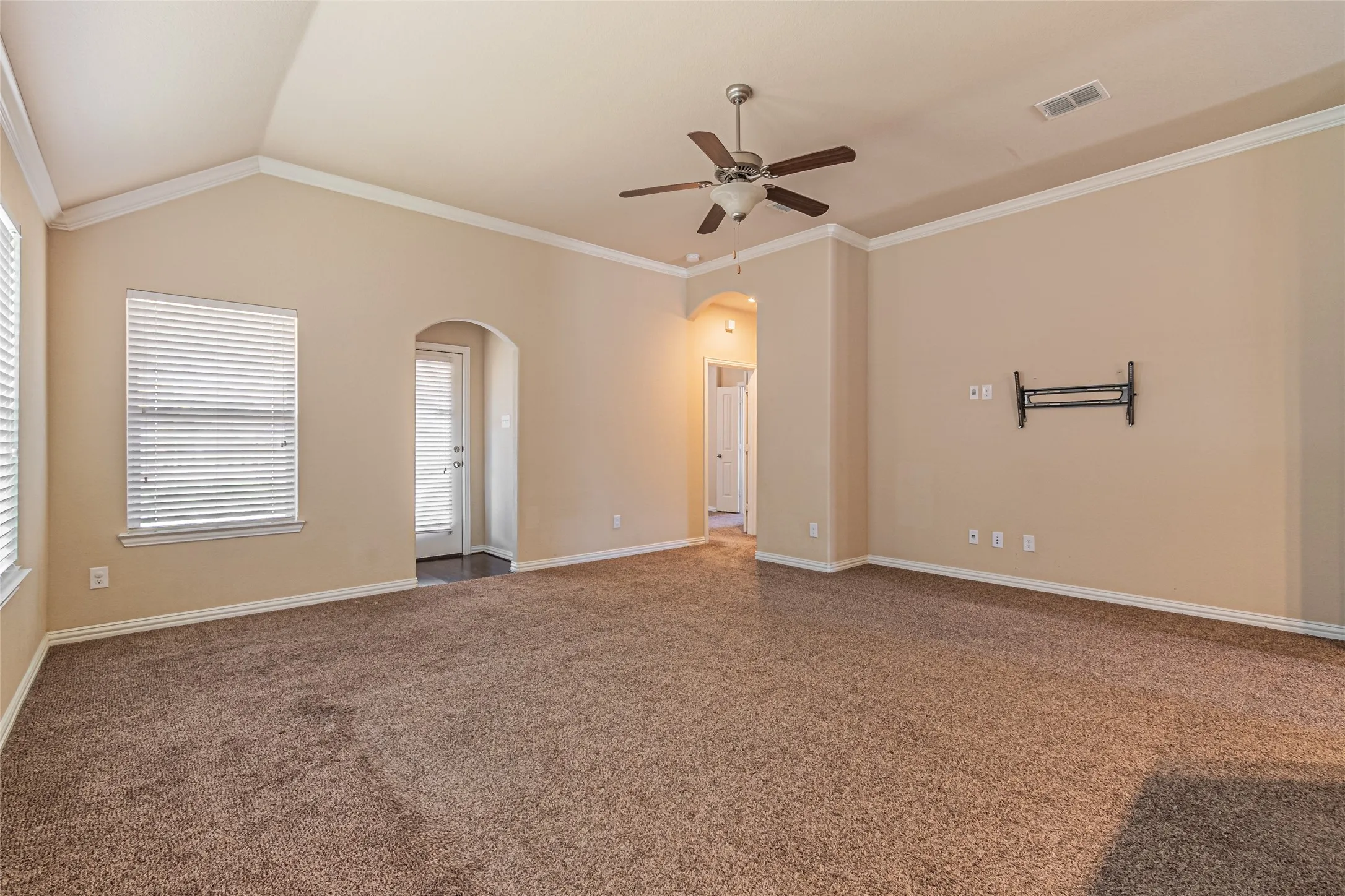 Vaulted ceilings, neutral wall tones, arched entryways, wall-mounted ceiling fan, and window blinds