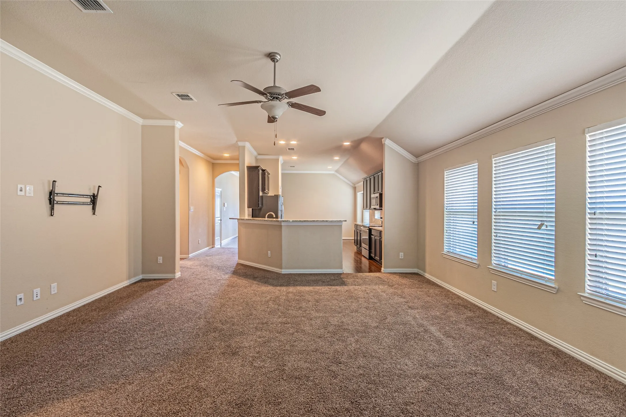 Open-concept interior featuring vaulted ceilings, crown molding, a ceiling fan, and a breakfast bar with stone-finish countertops